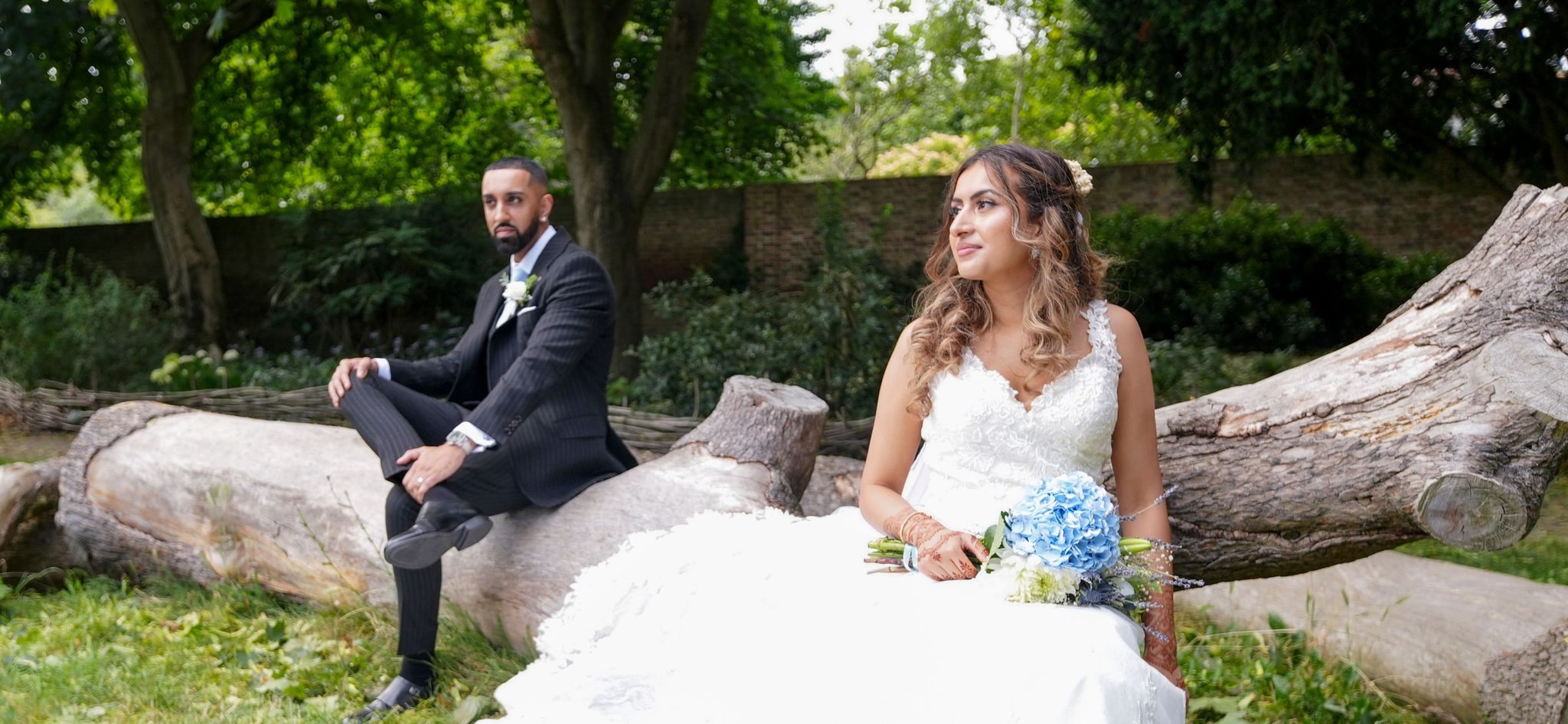 Bride and groom seated on fallen logs, her dress spilling over the wood