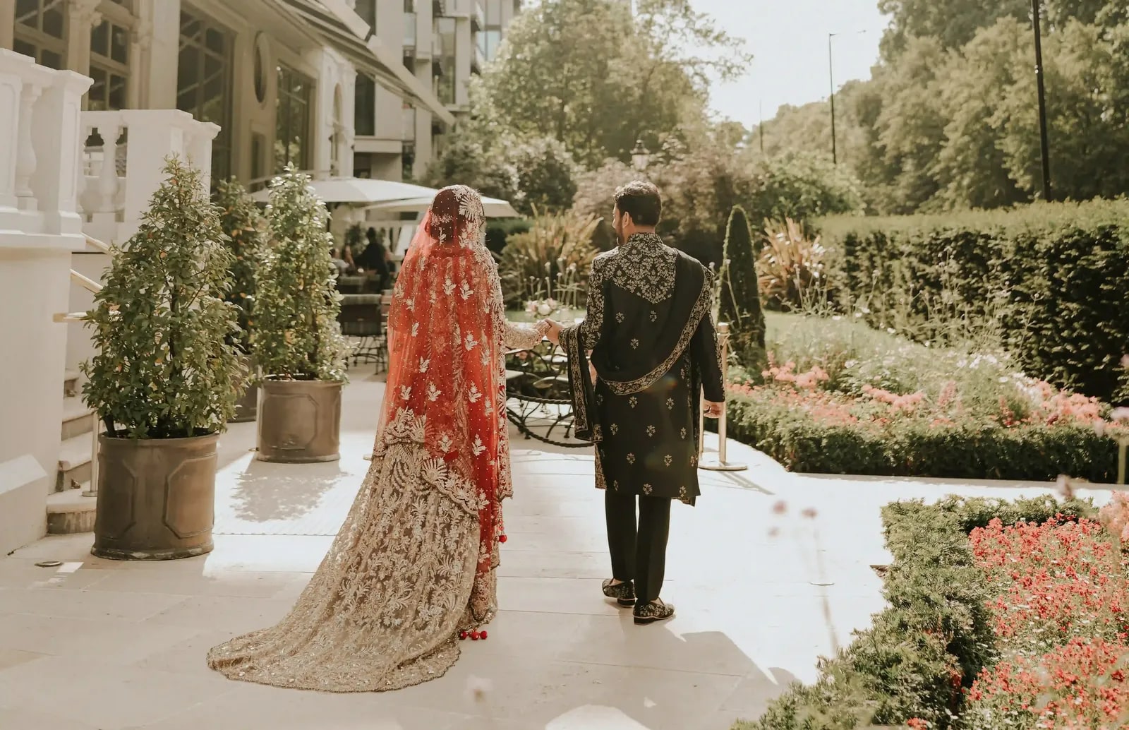 Couple walking away down a garden path, her long train sweeping the paving