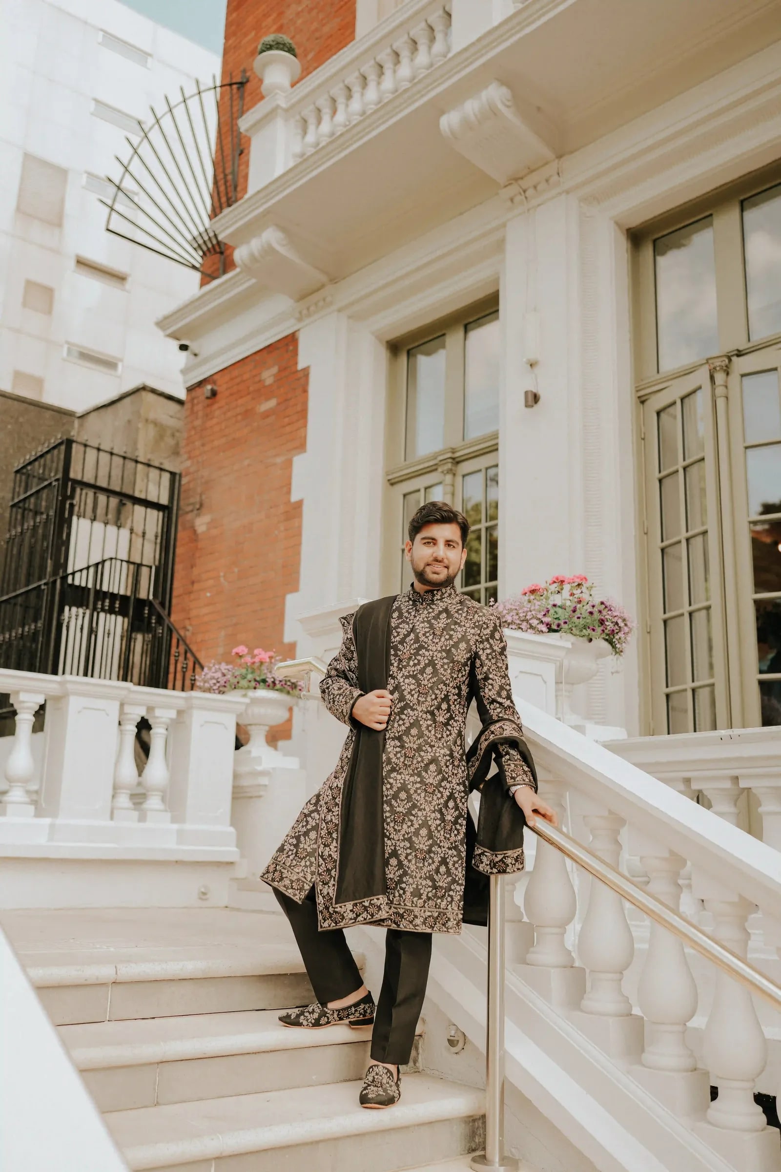 Groom alone on the hotel steps in a dark embroidered sherwani