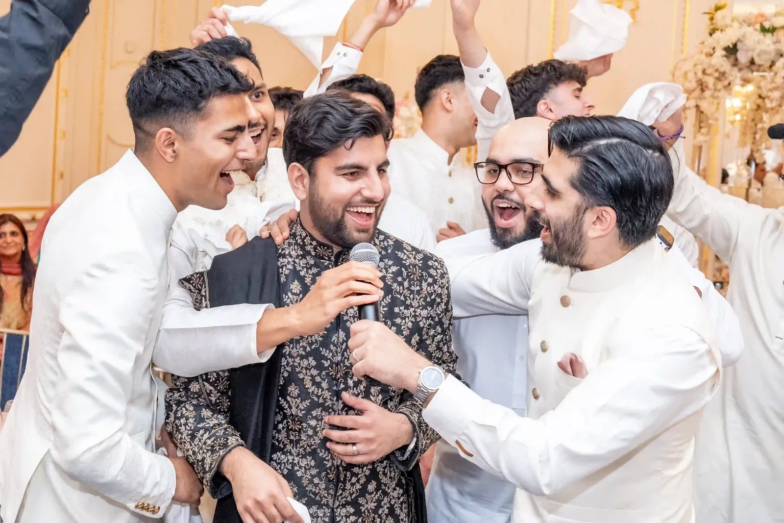 Friends crowding in around the groom, arms over his shoulders, as he sings