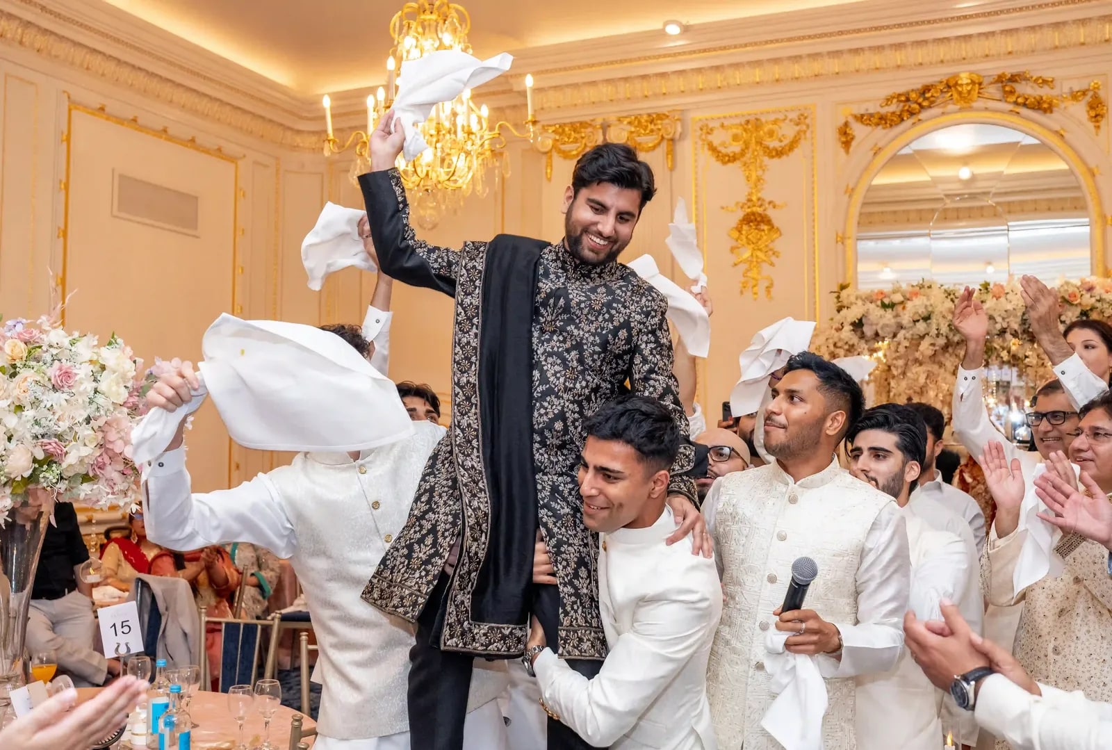 Groom lifted off his feet by a friend as the others cheer with napkins raised