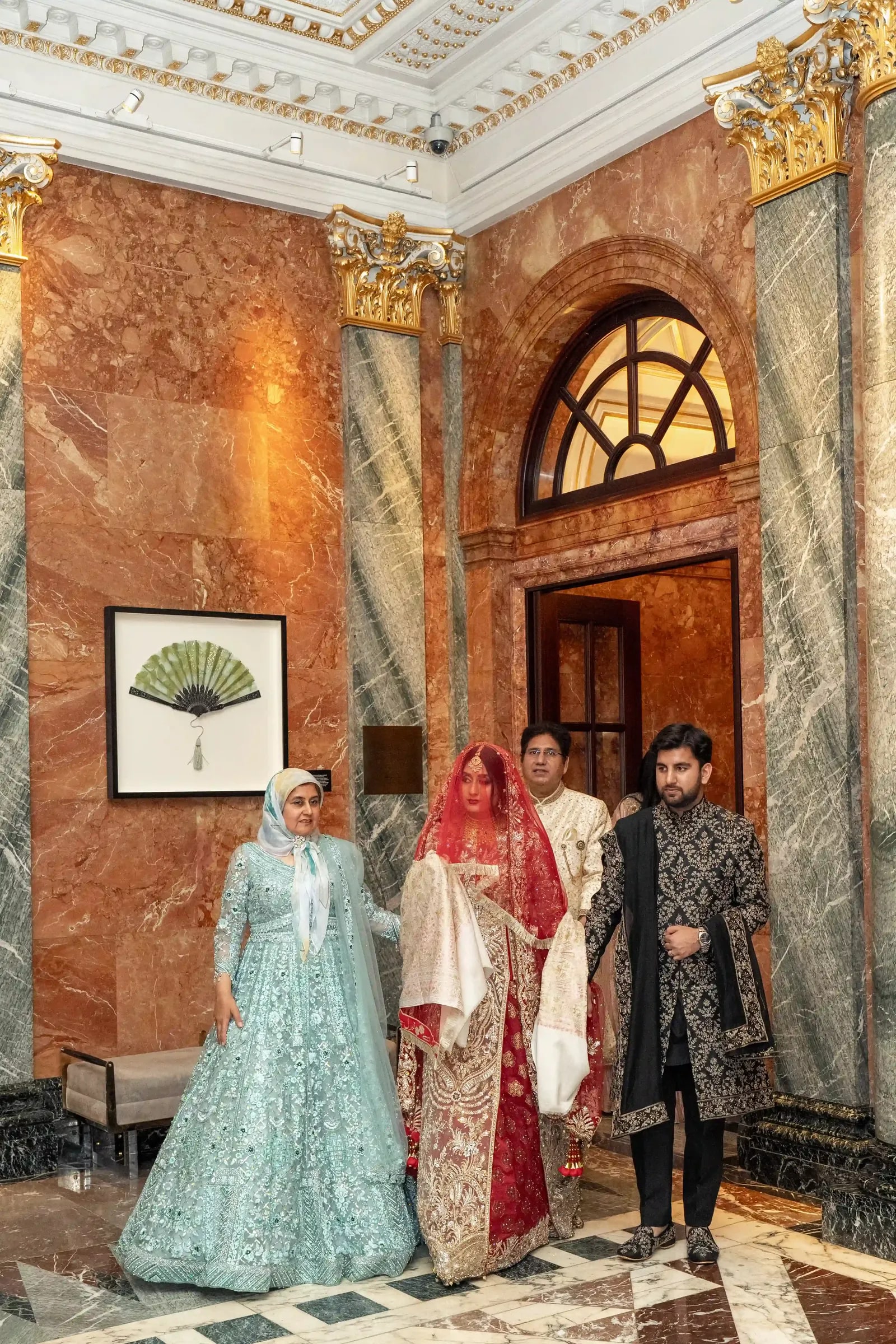 Bride walked through the marble hall by her family, her red dupatta over her head