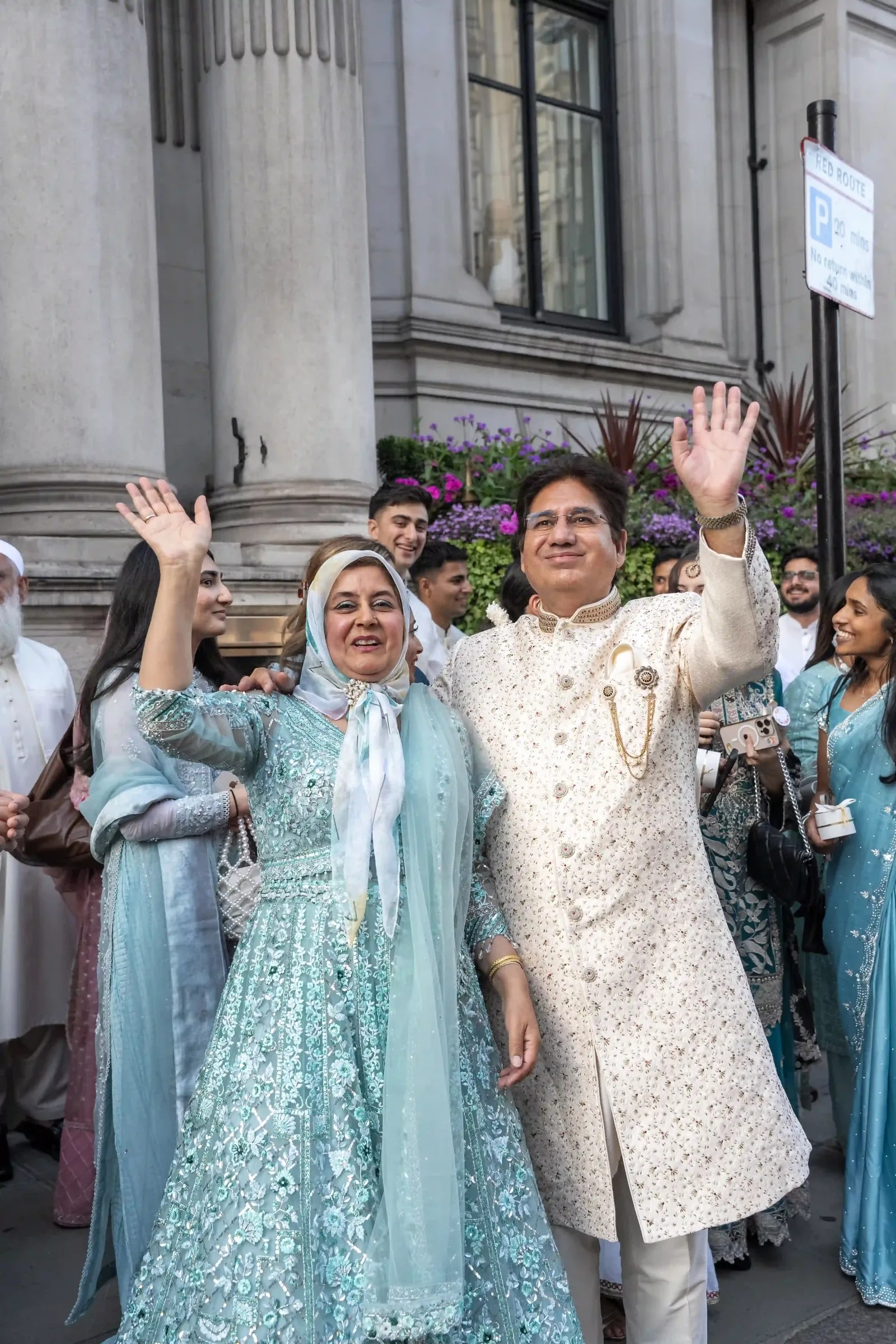 The groom's parents waving on the street as the baraat sets off
