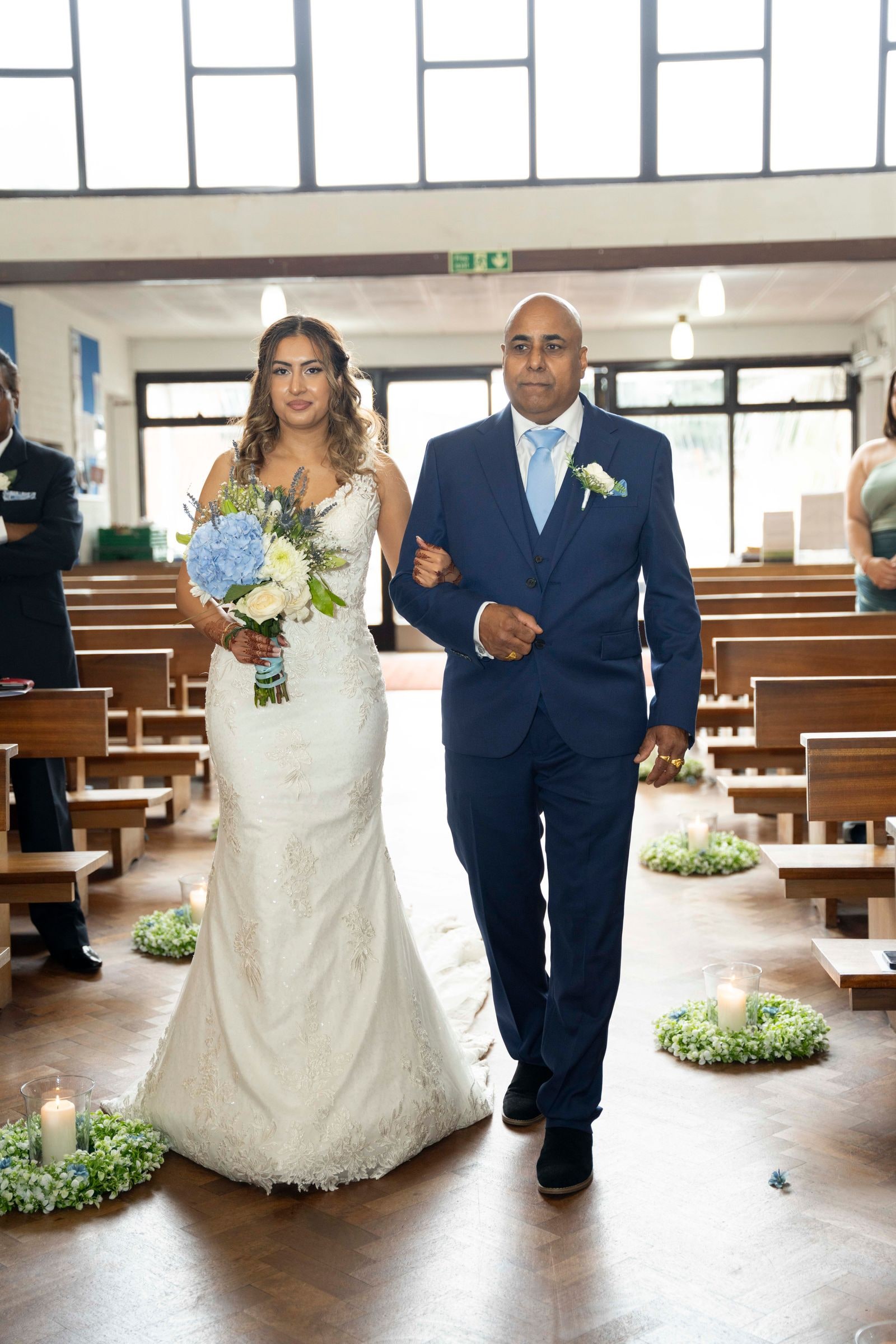 The bride walked down the church aisle on the arm of a man in a blue suit