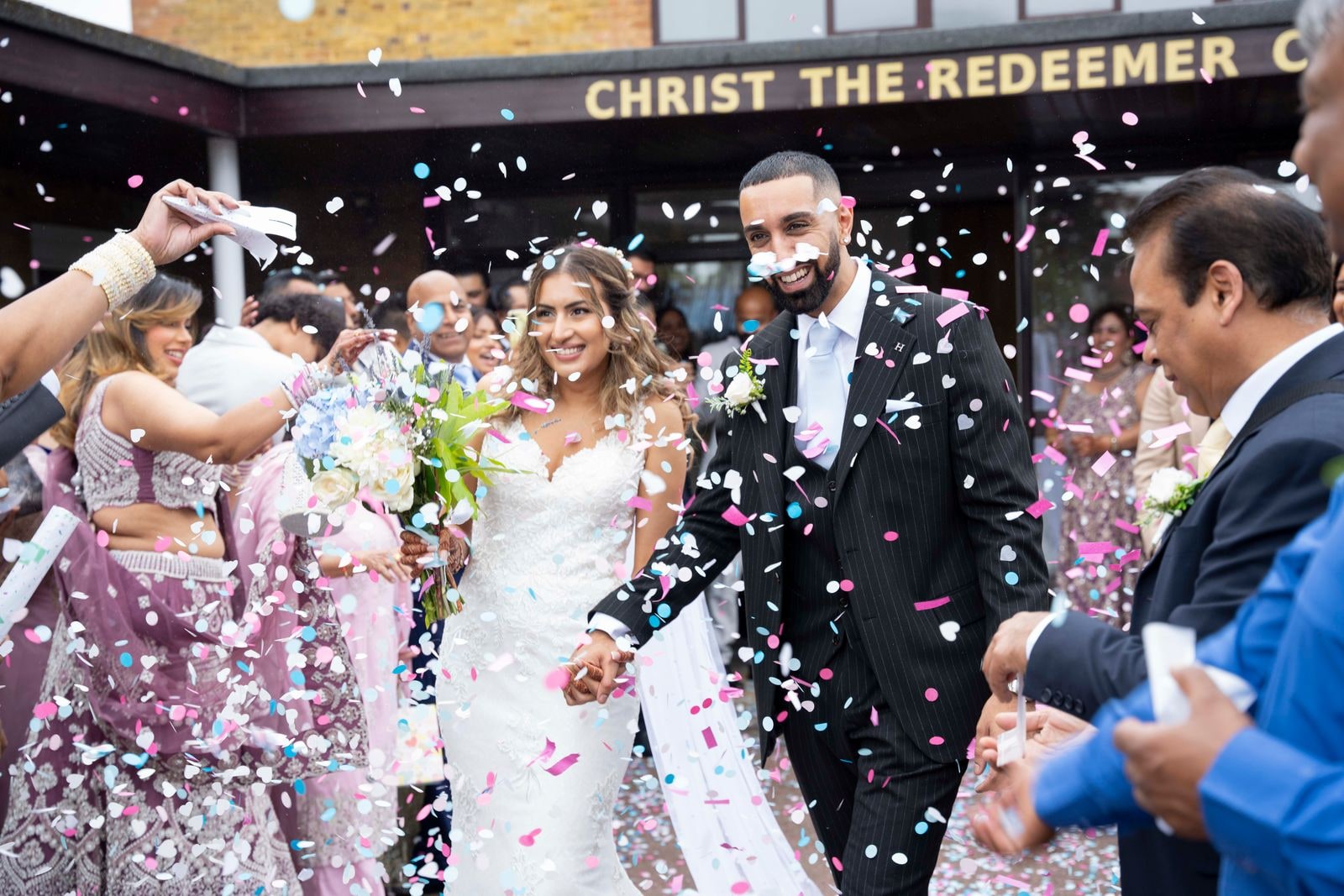 Bride and groom walking out through a shower of confetti, guests on both sides
