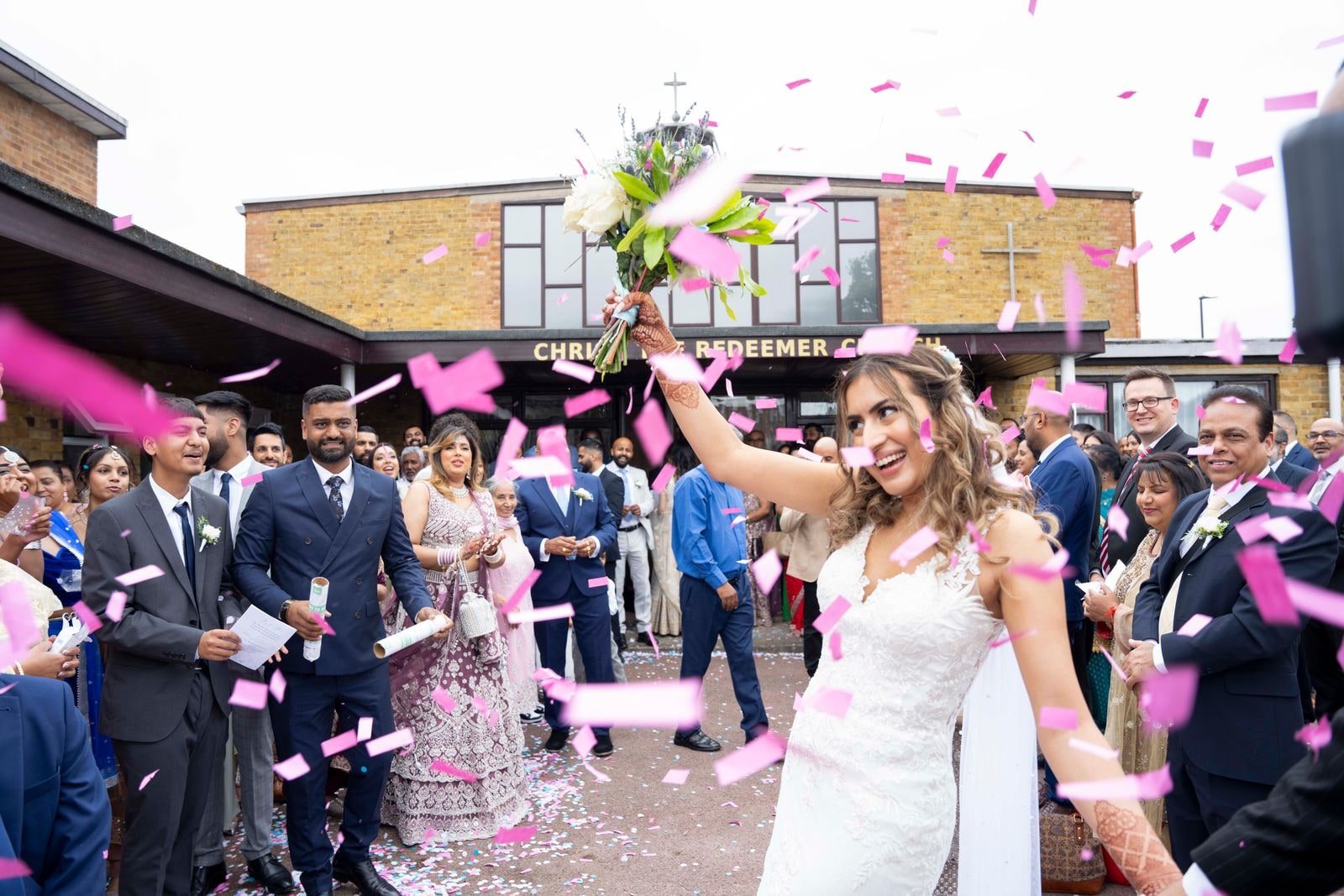 Bride raising her bouquet as confetti falls outside the church