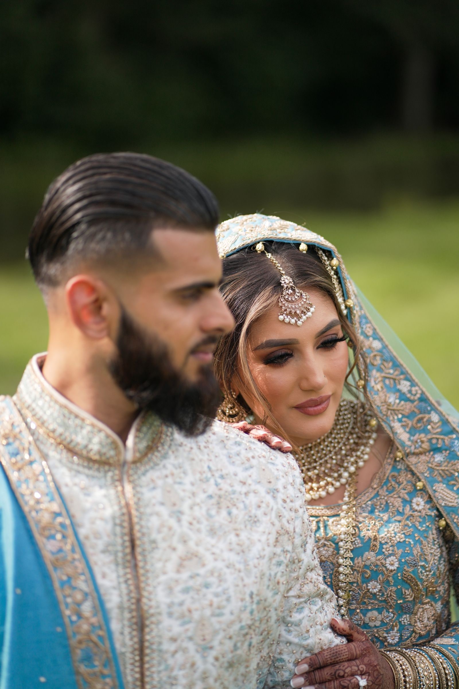 Groom holding his bride from behind, both in ivory and pale blue with gold embroidery
