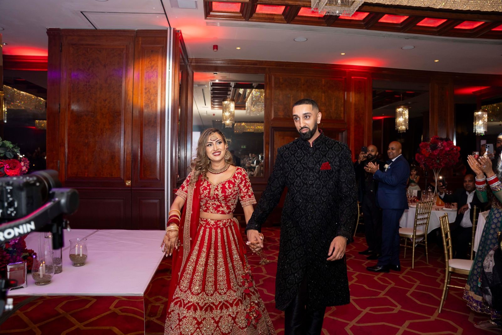 Bride in red and gold and groom in a black sherwani entering the reception