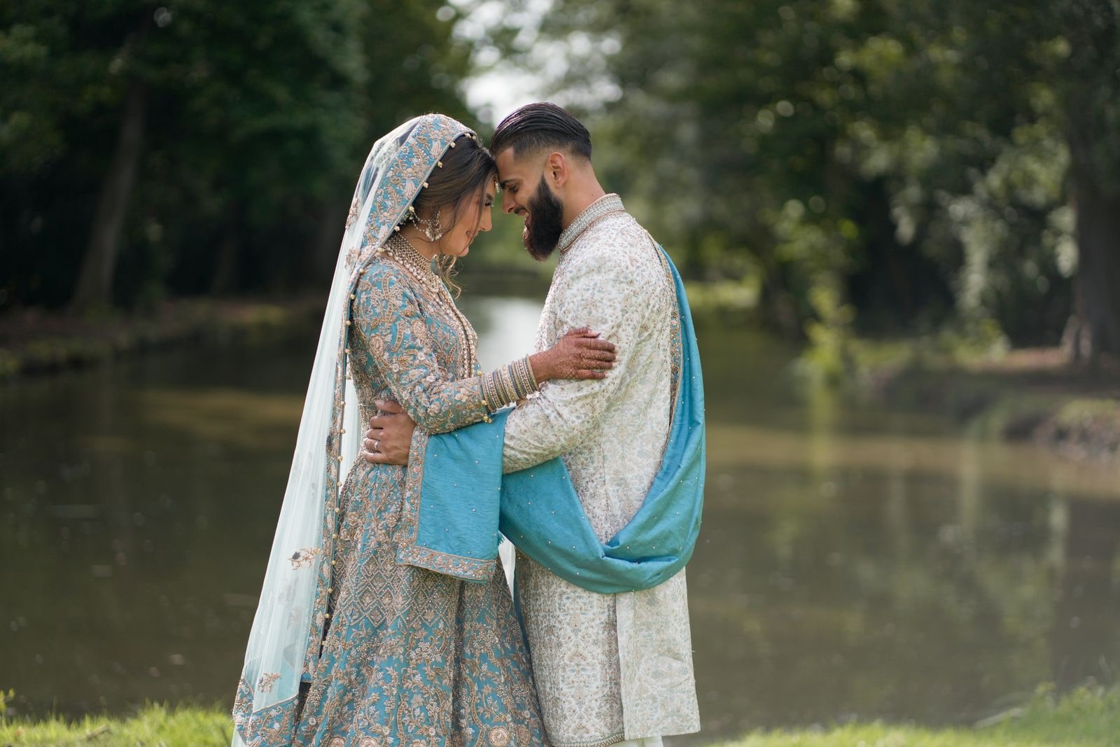 Couple forehead to forehead beside the lake at Warbrook House, her blue dupatta falling around them
