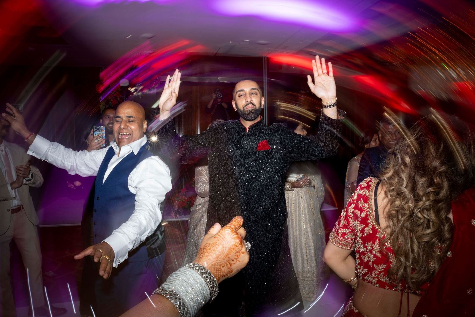 Groom dancing with his hands up, the room streaked with coloured light