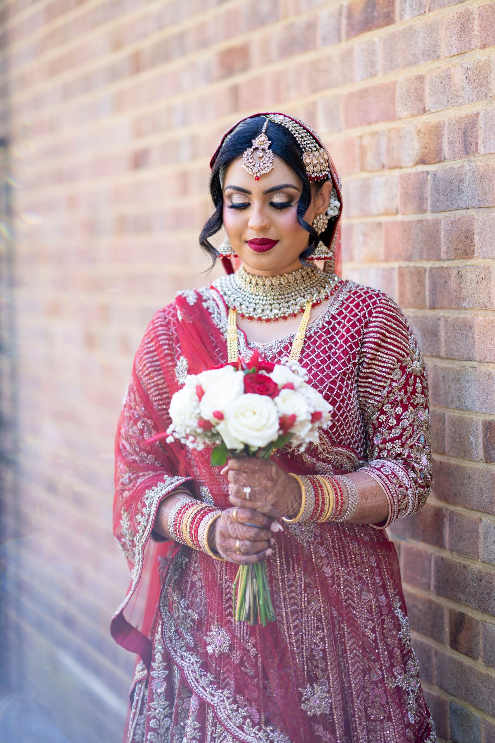 Bride against a brick wall holding a white bouquet, eyes lowered