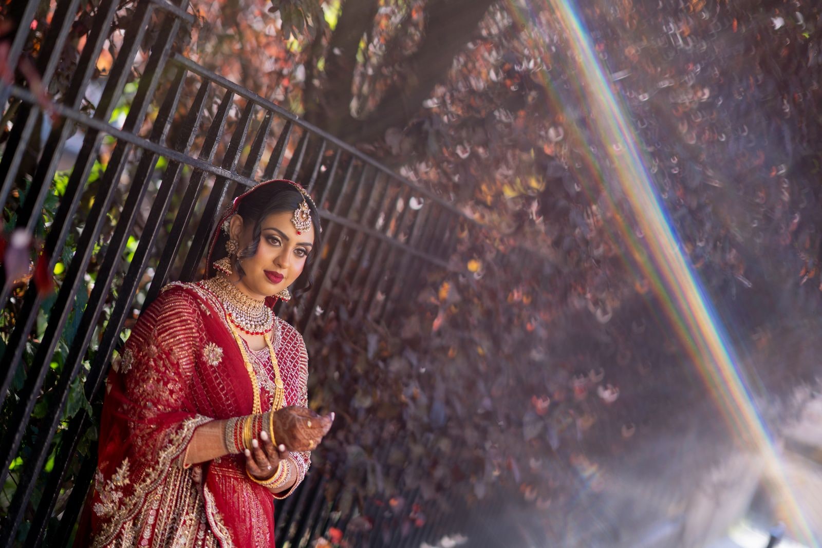Bride against iron railings in red and gold, autumn leaves behind her