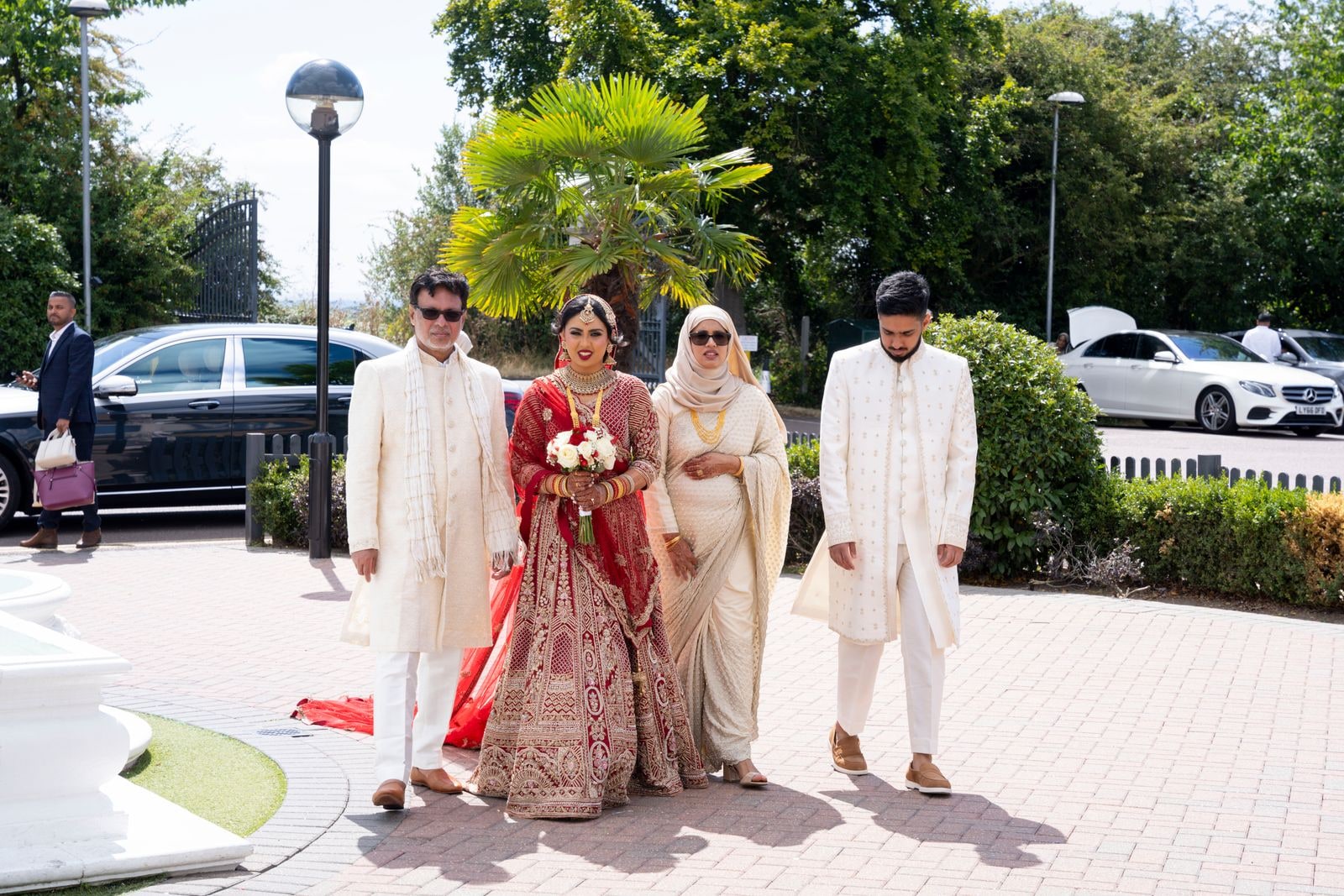 The bride's family walking her towards the venue, her red train trailing behind
