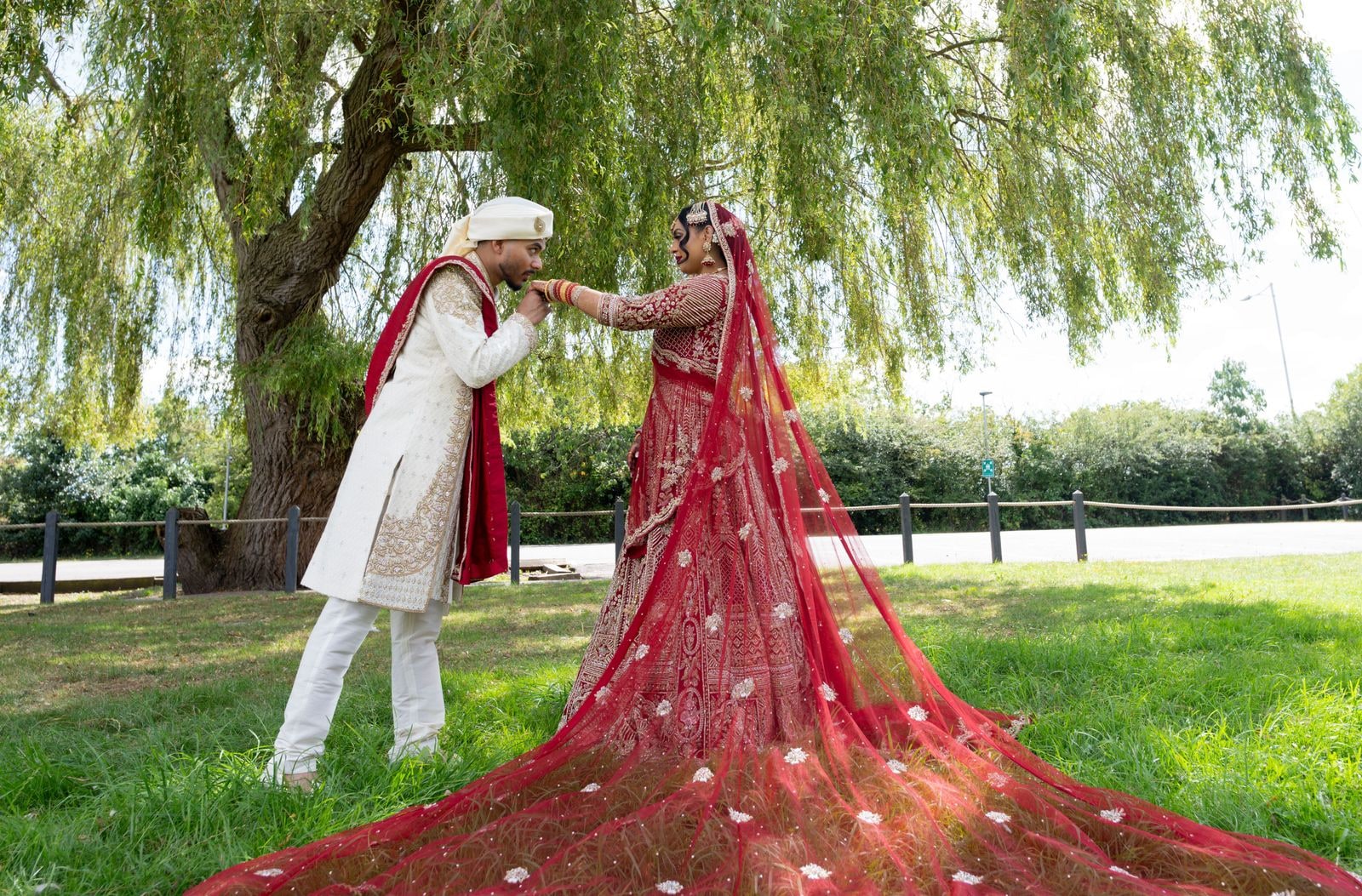 Couple beneath a willow, the bride's red train fanned out in a full circle on the grass