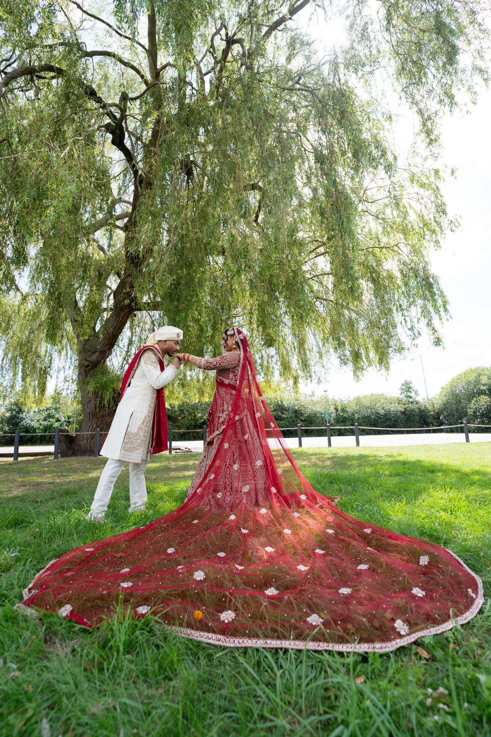 Couple beneath a willow, the bride's red train fanned out in a full circle on the grass