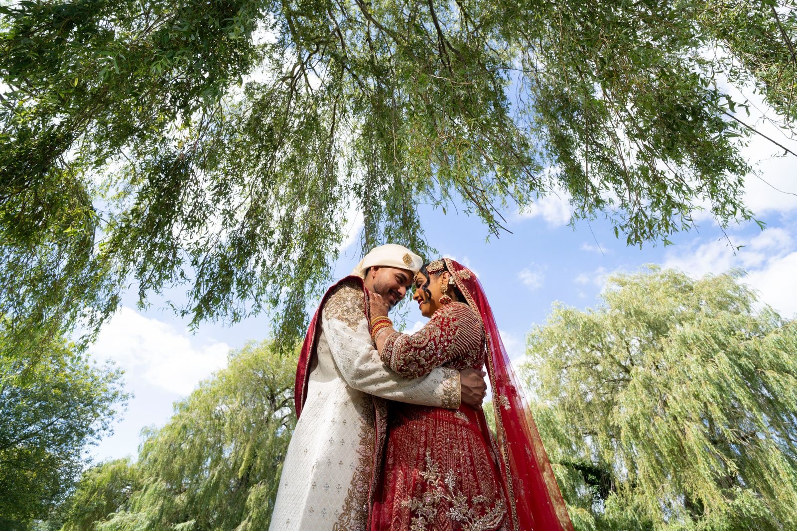 Couple close together beneath the willow branches, seen from below against the sky