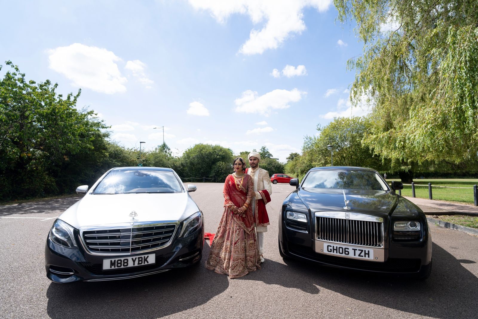 Bride standing between a white Mercedes and a black Rolls-Royce on the road