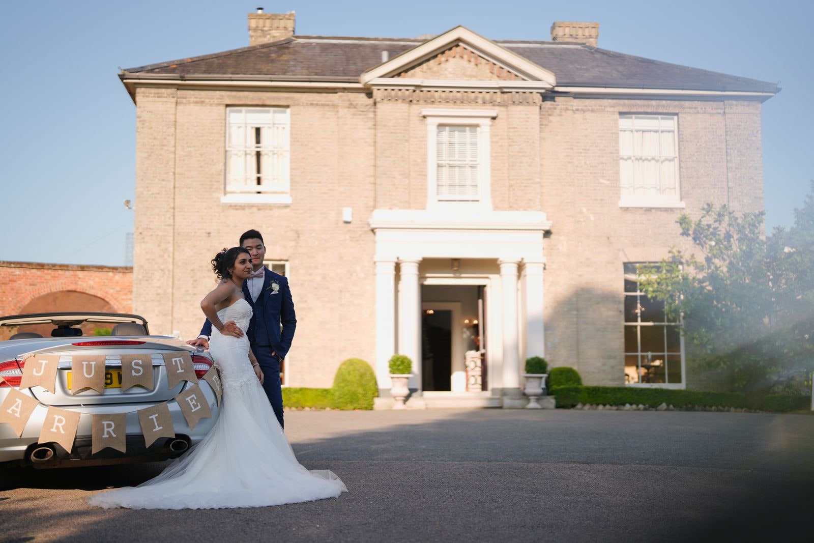 Bride and groom beside the Just Married car outside the front of the house