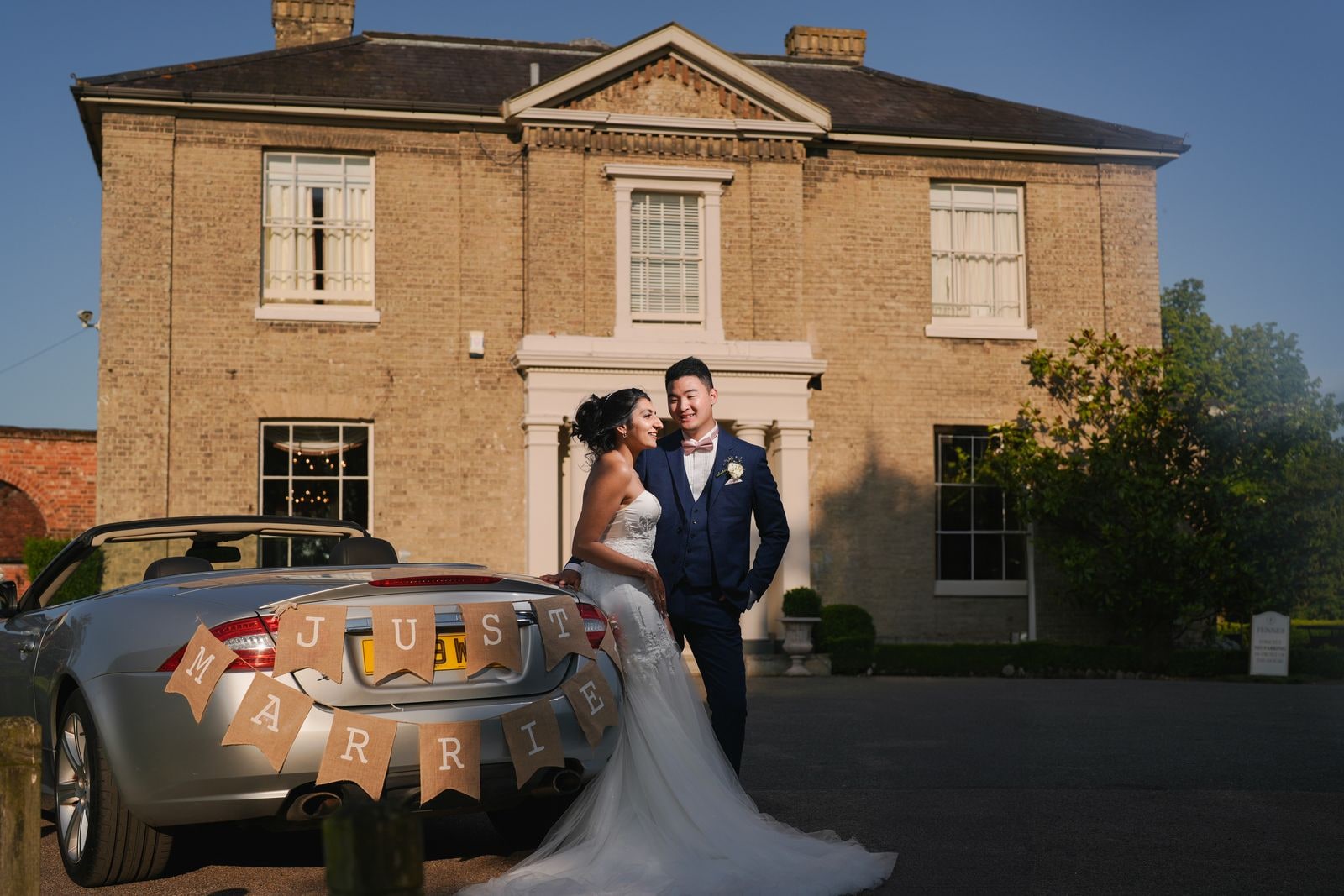 Bride and groom by the car at dusk, the house lit behind them
