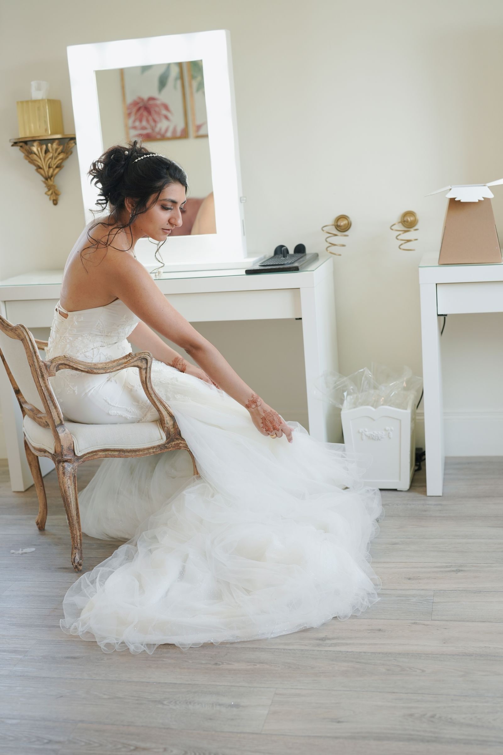 Bride seated at a dressing table arranging her train, in a quiet moment before the ceremony