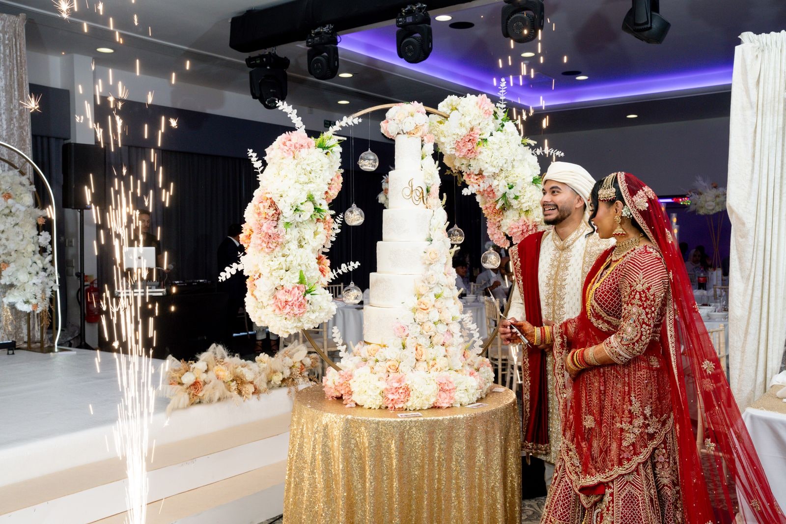 Couple cutting the flowered cake between two fountains of indoor sparks
