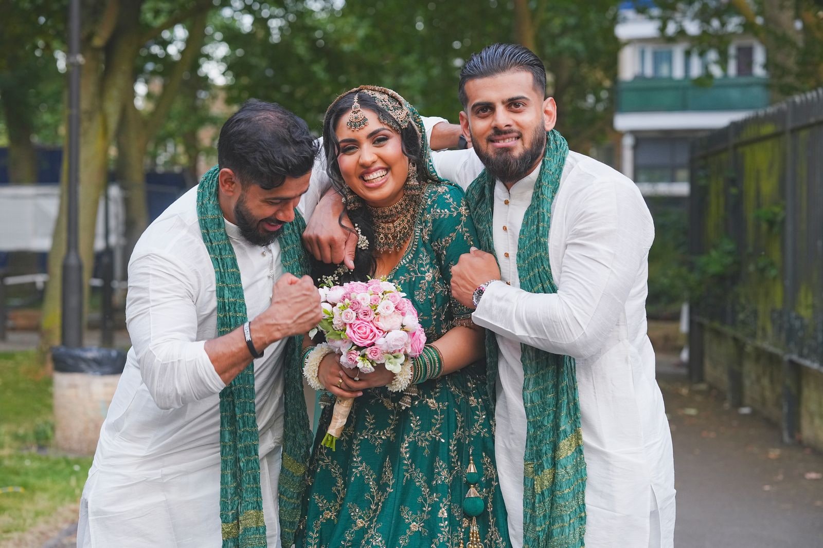 Bride in teal laughing between two men in white kurtas and green scarves