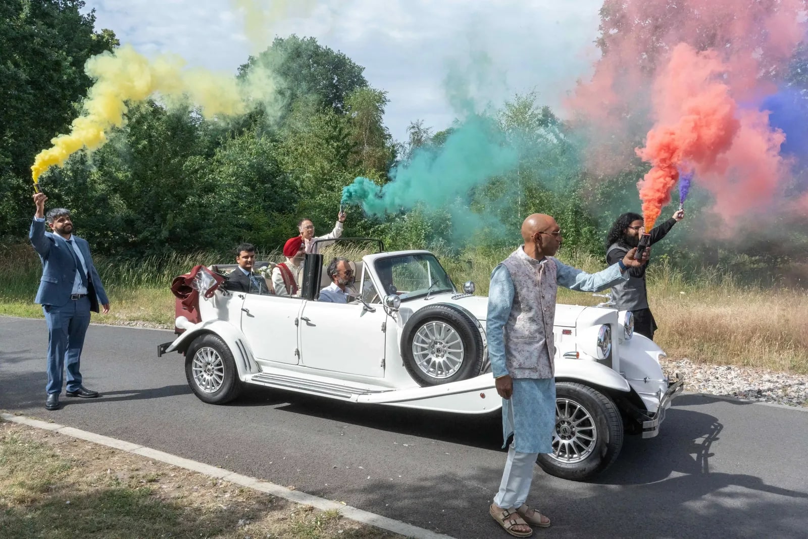 The groom arriving in a white vintage convertible, coloured smoke flares on both sides