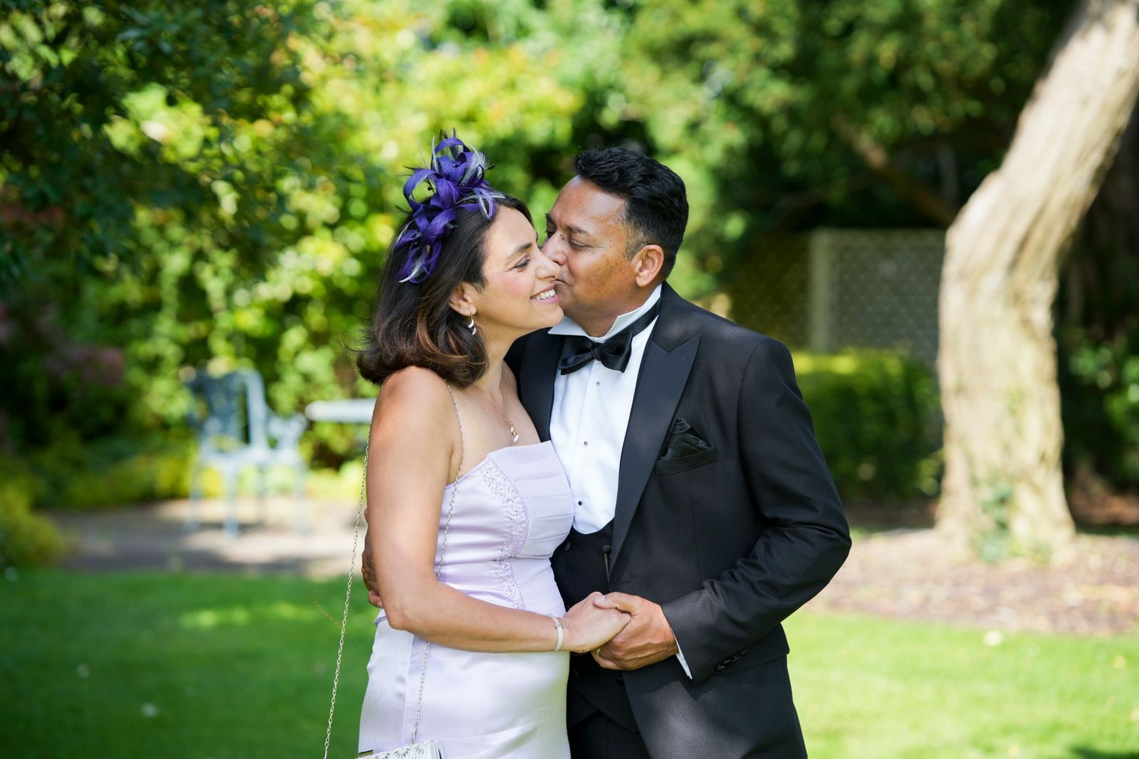 Guests in a fascinator and black tie holding each other in the garden