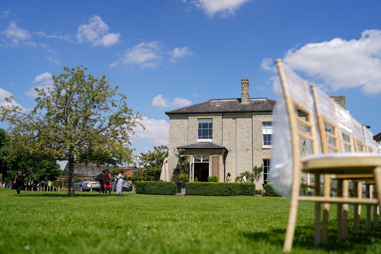 The house and lawn on a bright day, chairs being set out for the ceremony