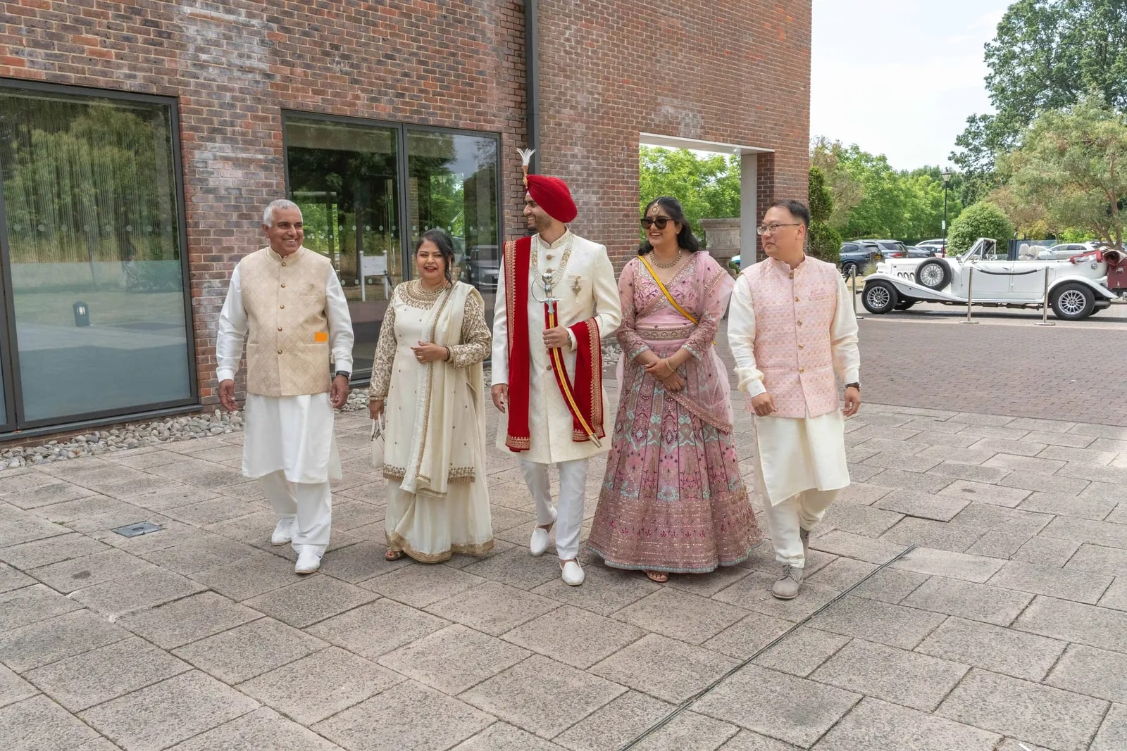 Groom walked in by his family across the paving, the vintage car behind them
