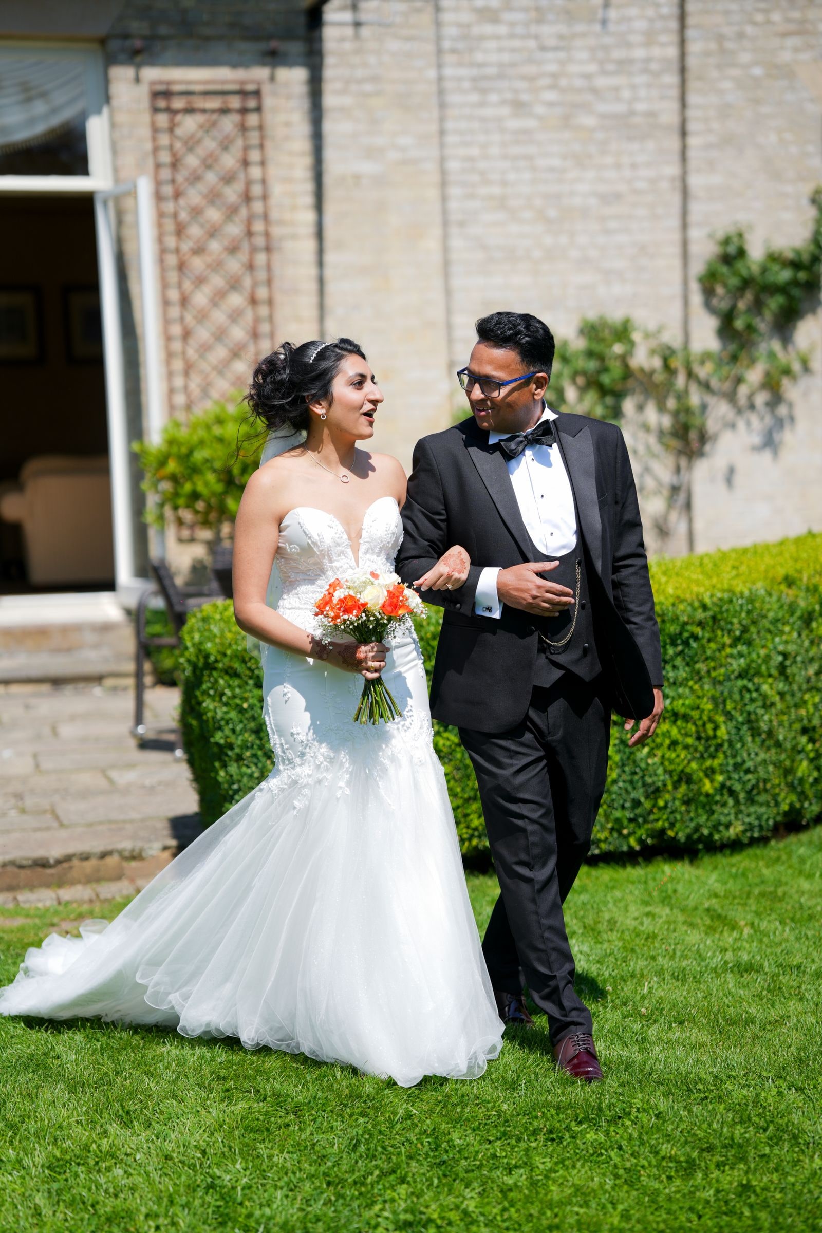 Bride carrying an orange bouquet walking across the grass with her groom