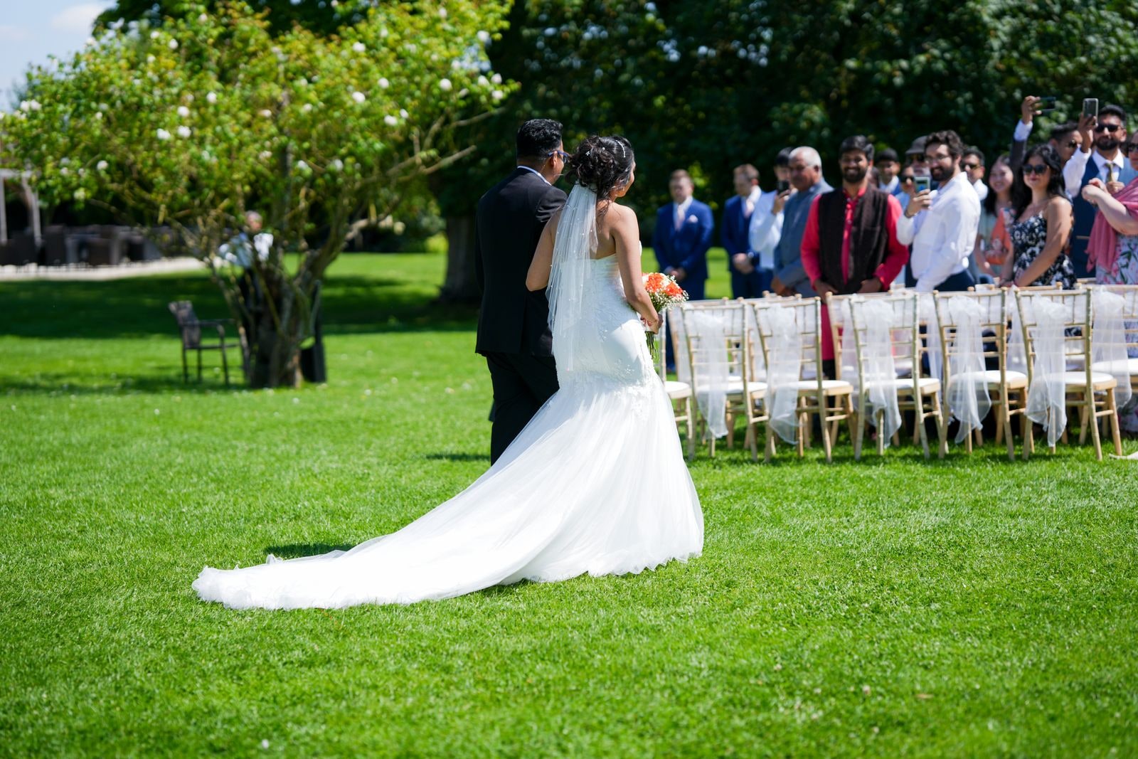 Bride's train trailing on the grass as she and her groom face the seated guests