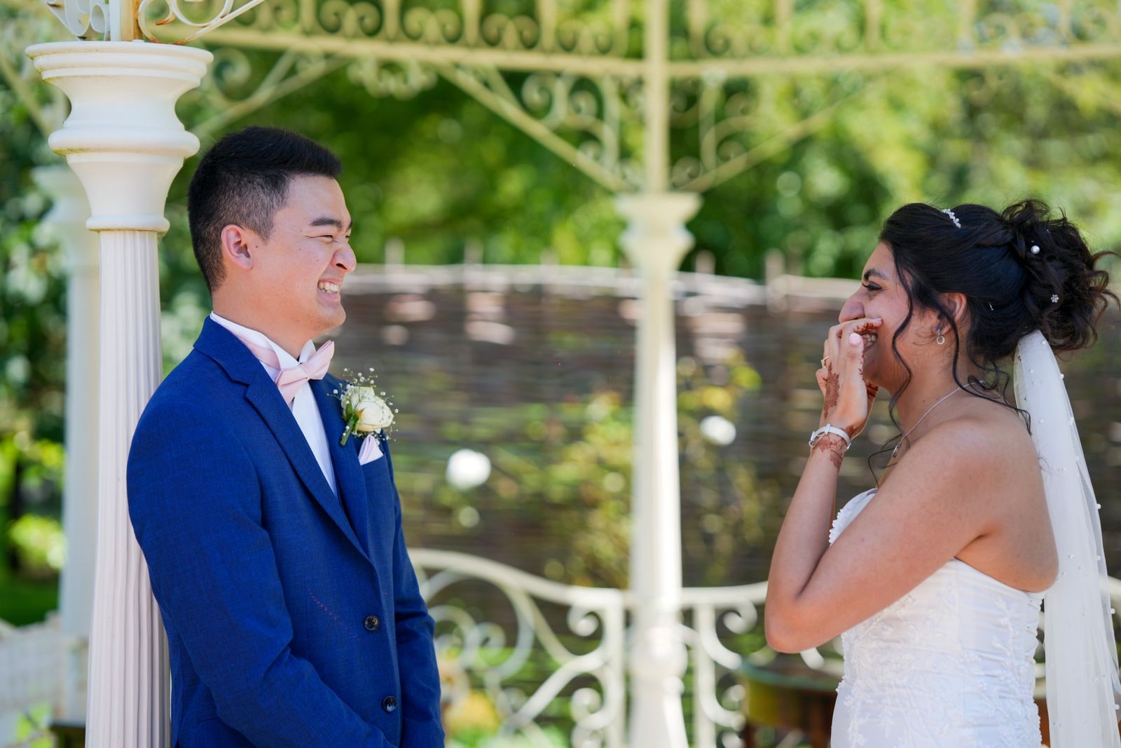 Bride laughing behind her hand as her groom grins at her under the bandstand