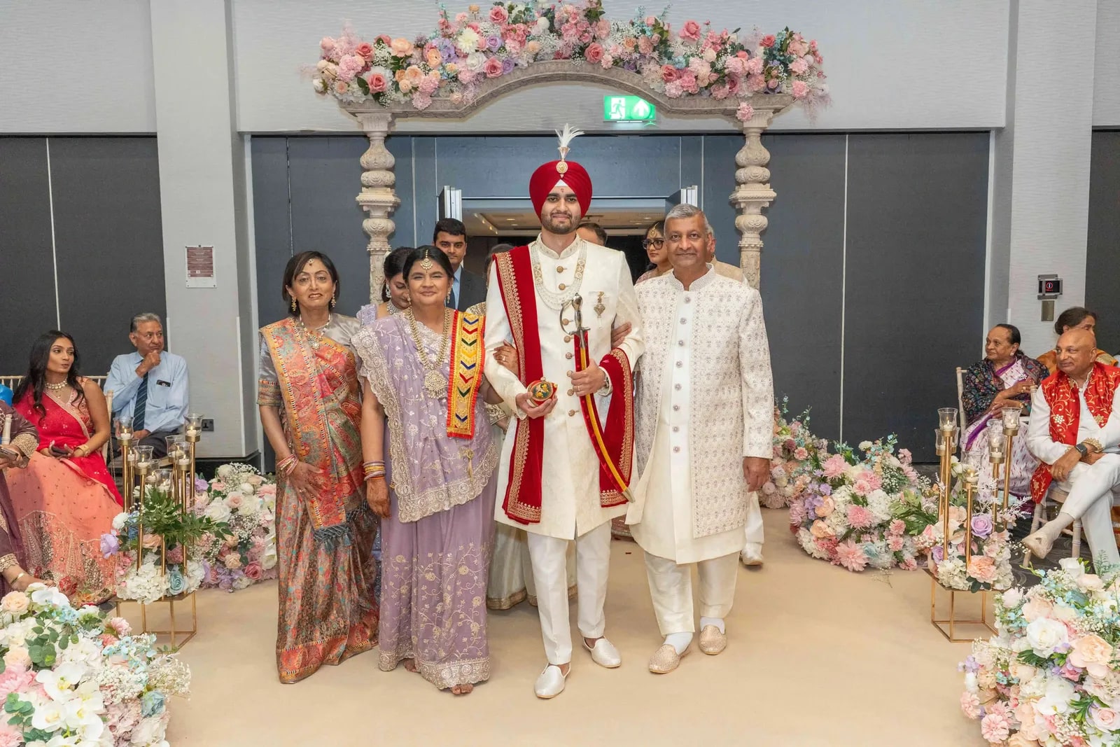 Groom standing with his family beneath the pastel flowered mandap