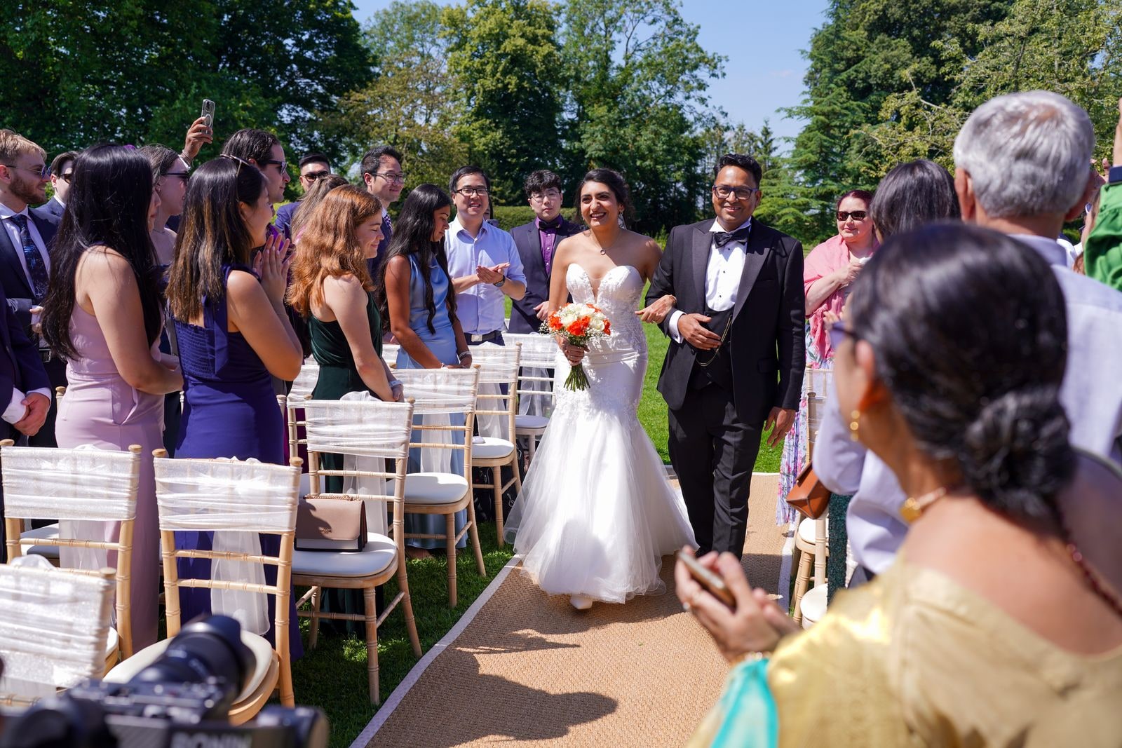 Bride and groom walking back down the aisle as guests applaud and film them
