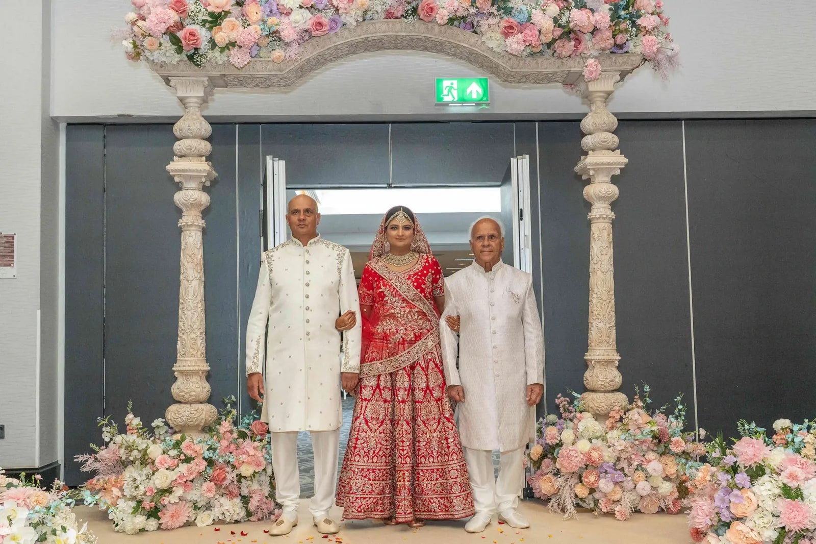 The bride walked in by two men in ivory between the mandap pillars