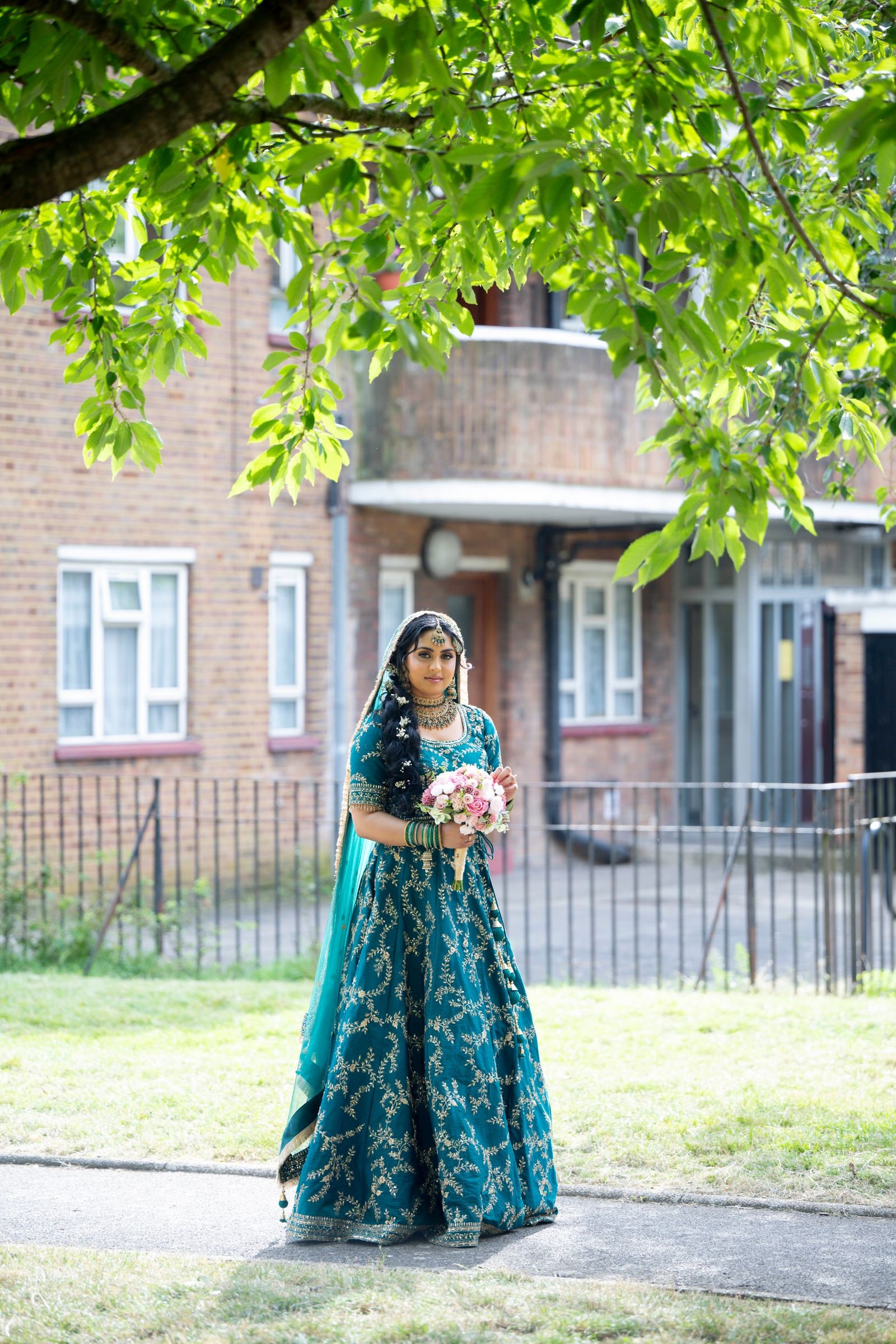 Bride in teal holding a bouquet under a chestnut tree on a London street