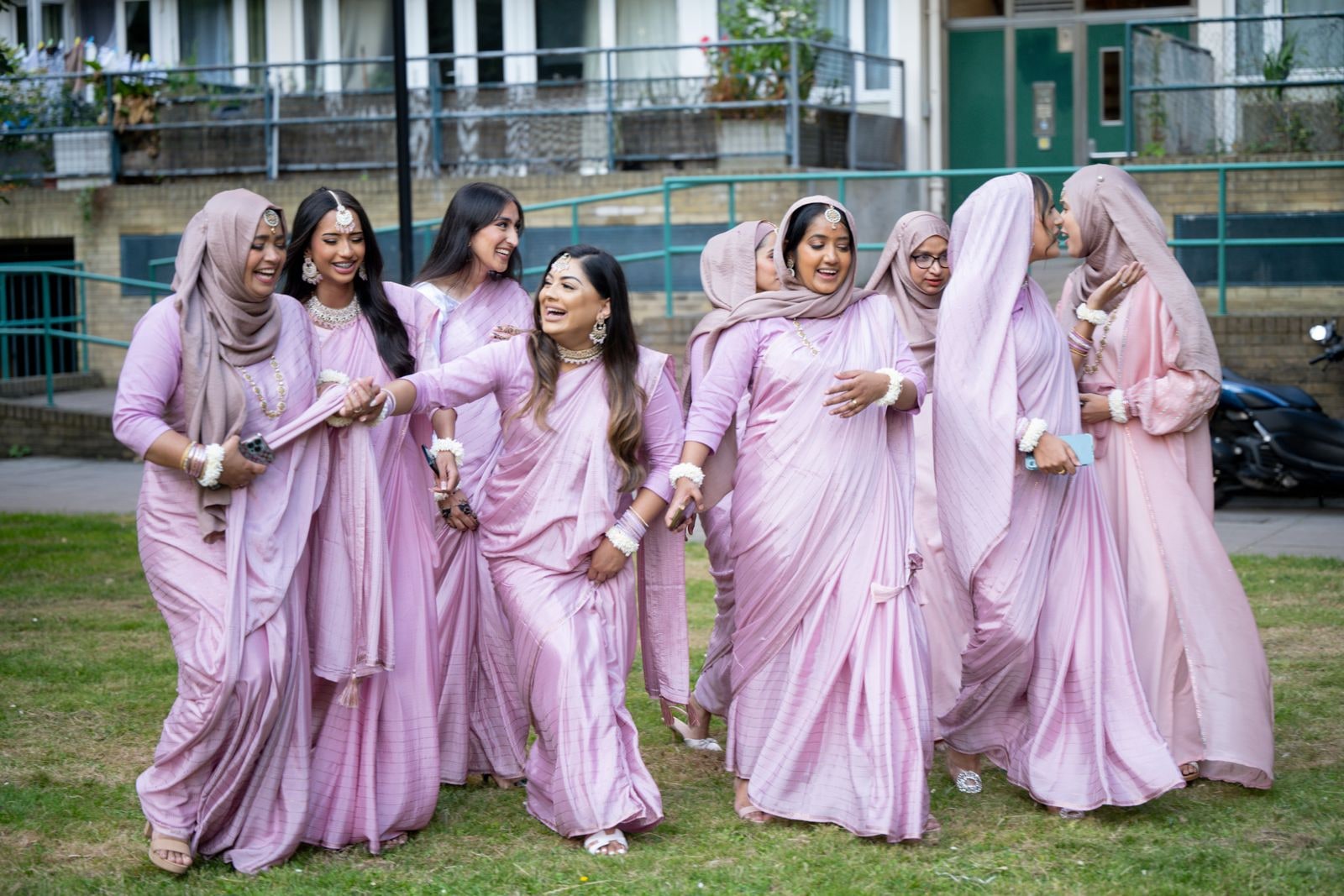 The bride's party in pink saris walking together across the green