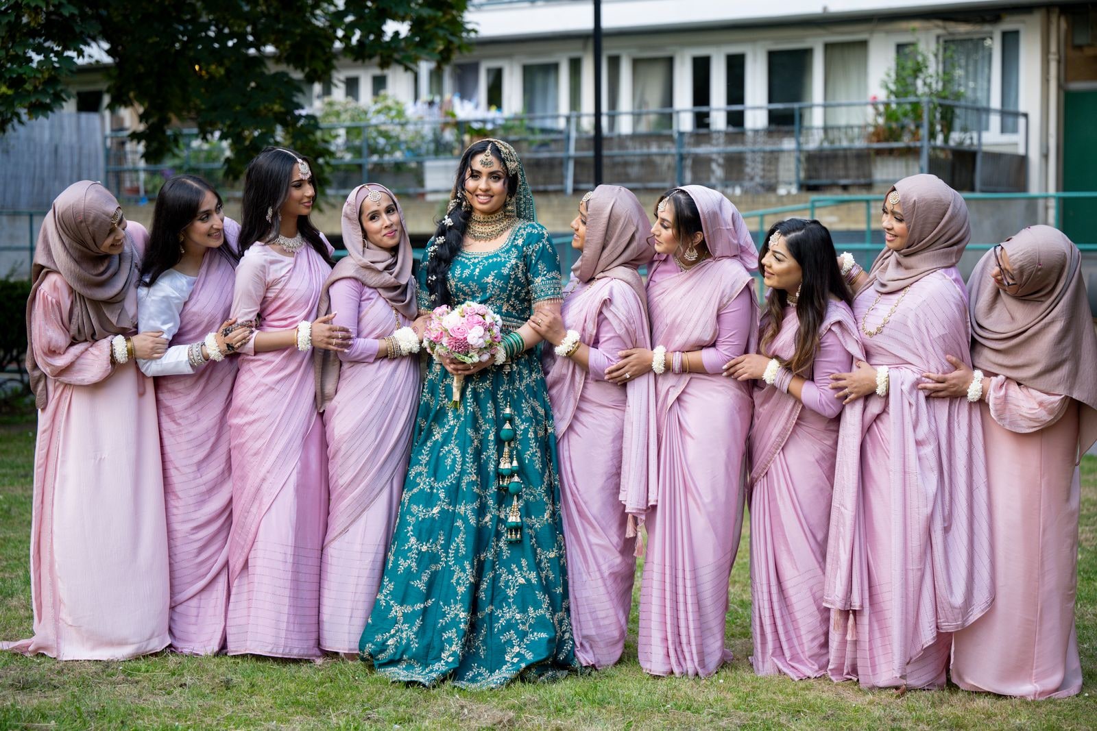 Bride in teal surrounded by her friends in pink, all linked arm in arm