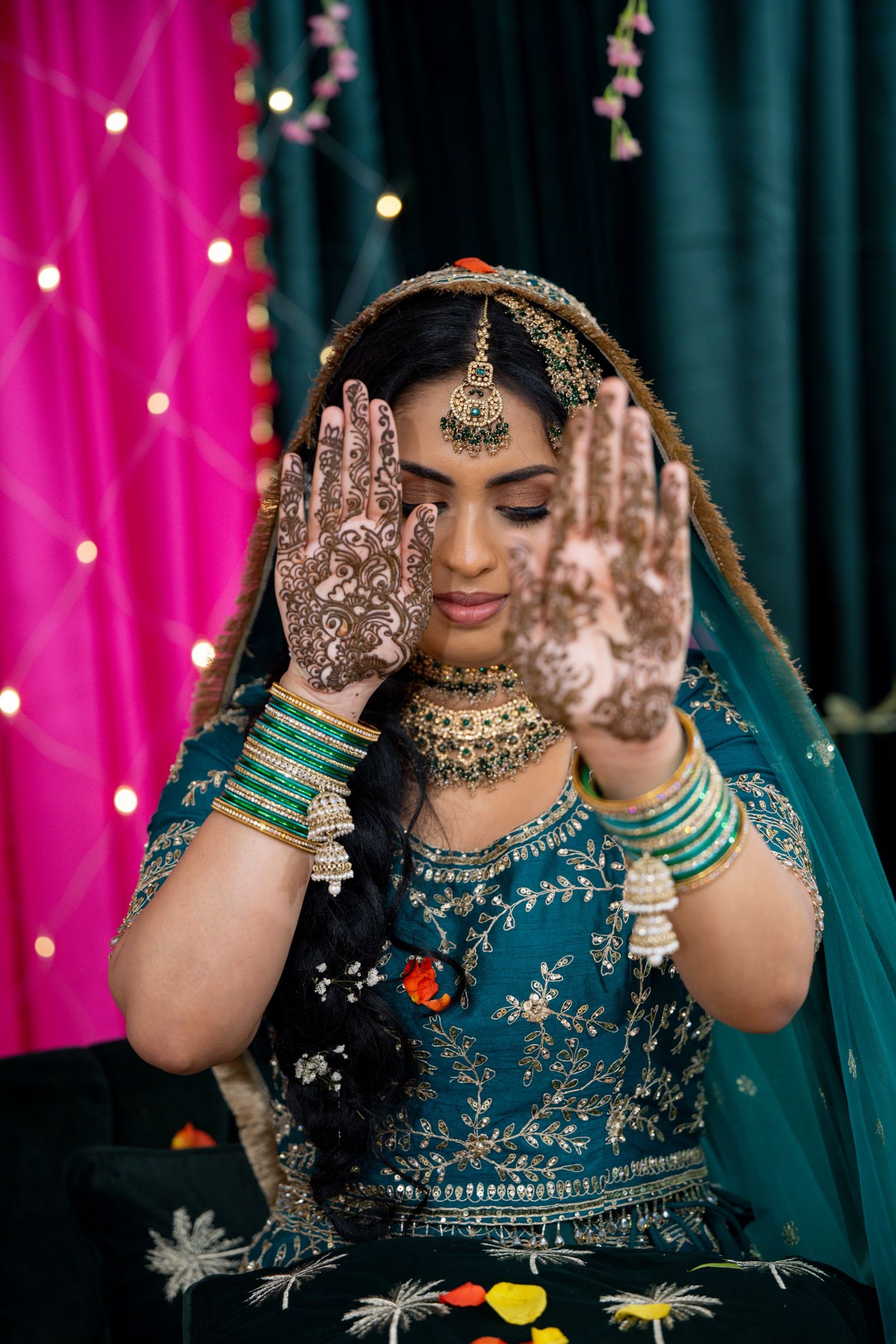 Bride holding up her hennaed palms at the mehndi, in teal and gold