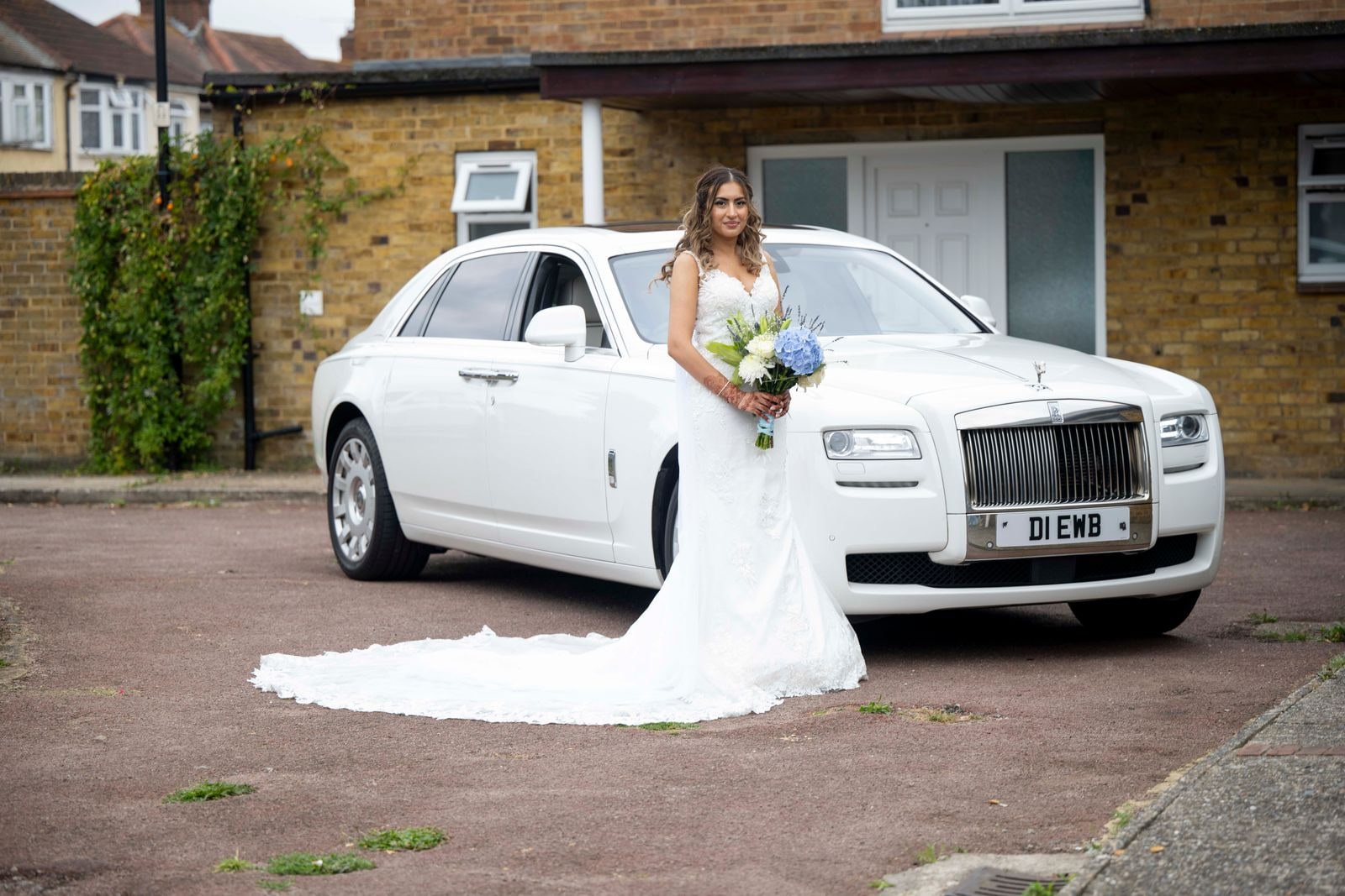 Bride standing beside a white Rolls-Royce, her train spread on the ground