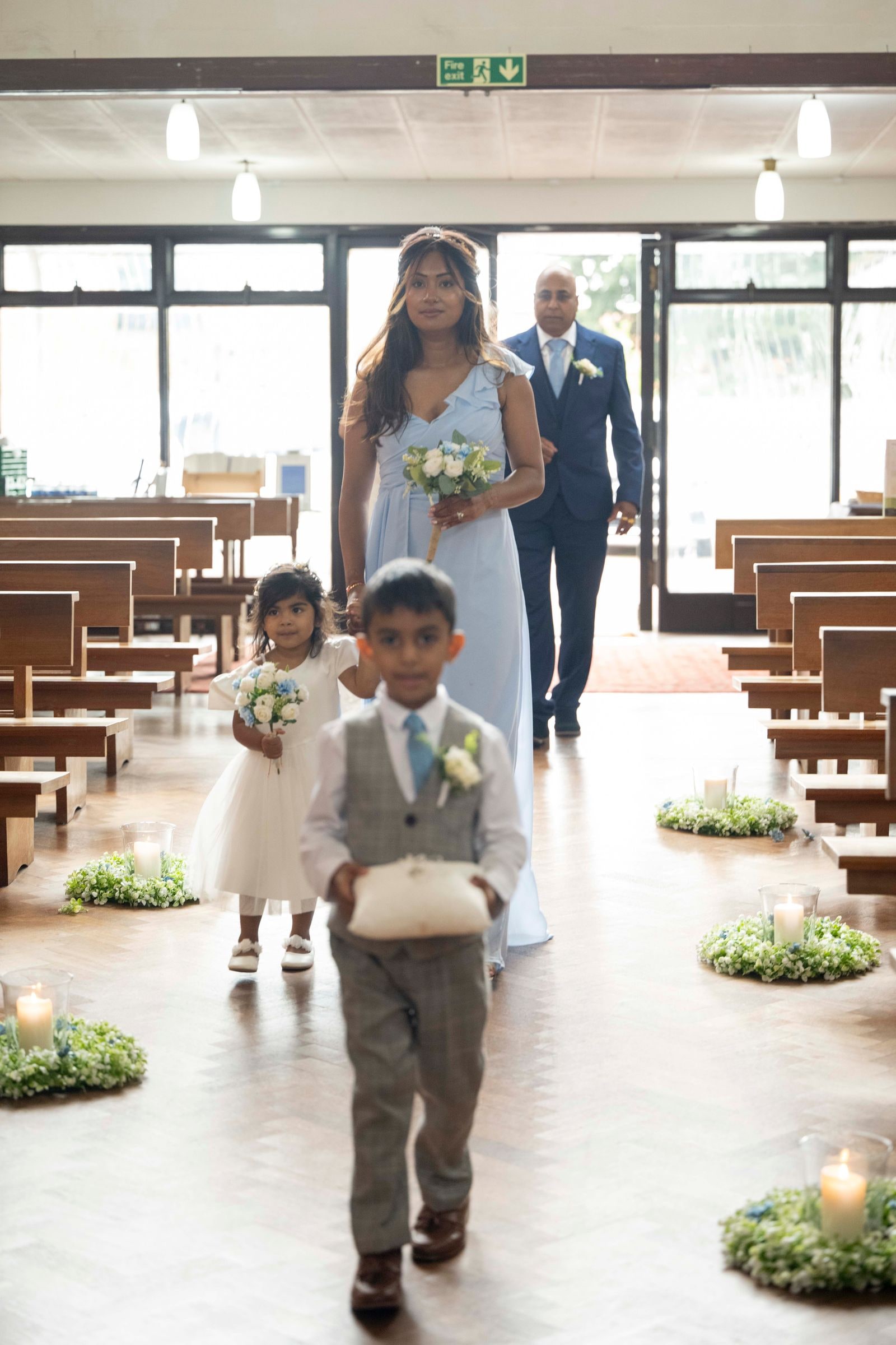 A pageboy and flower girl walking up the aisle ahead of the bride