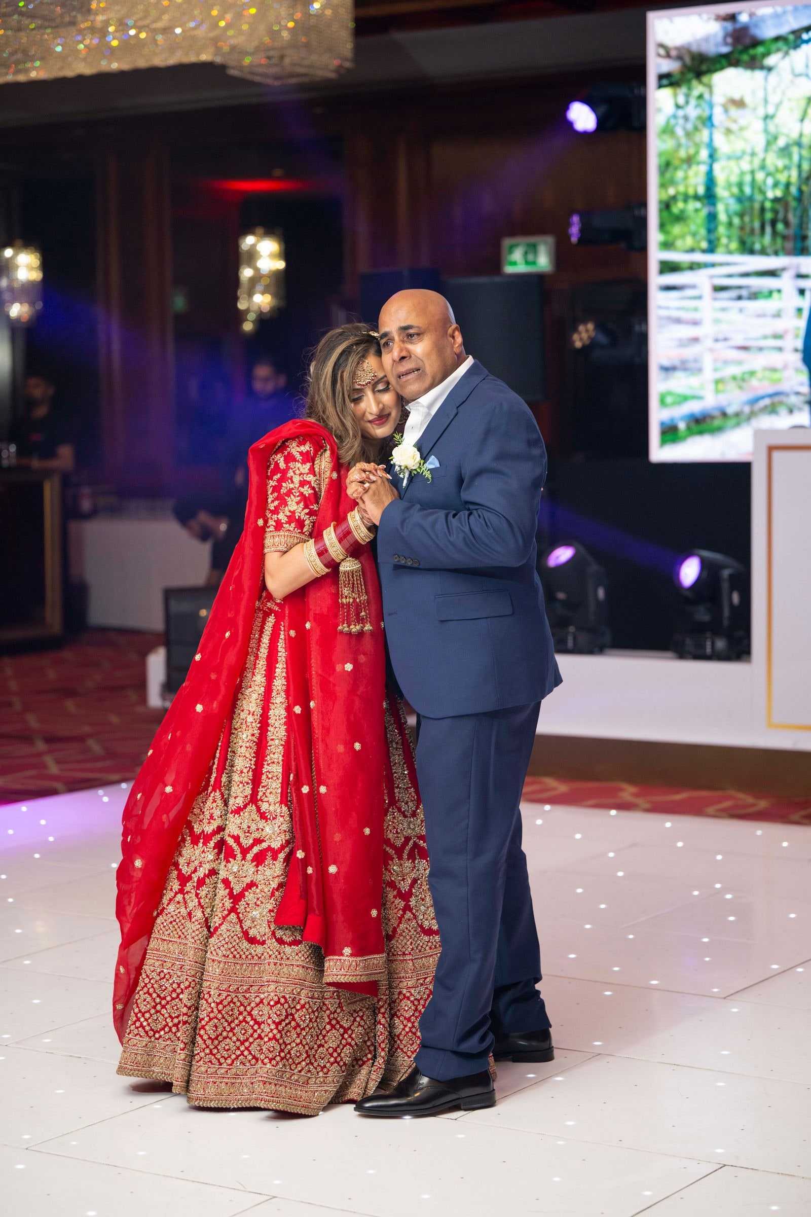 Bride in a red and gold lehenga dancing with a guest under the reception lights