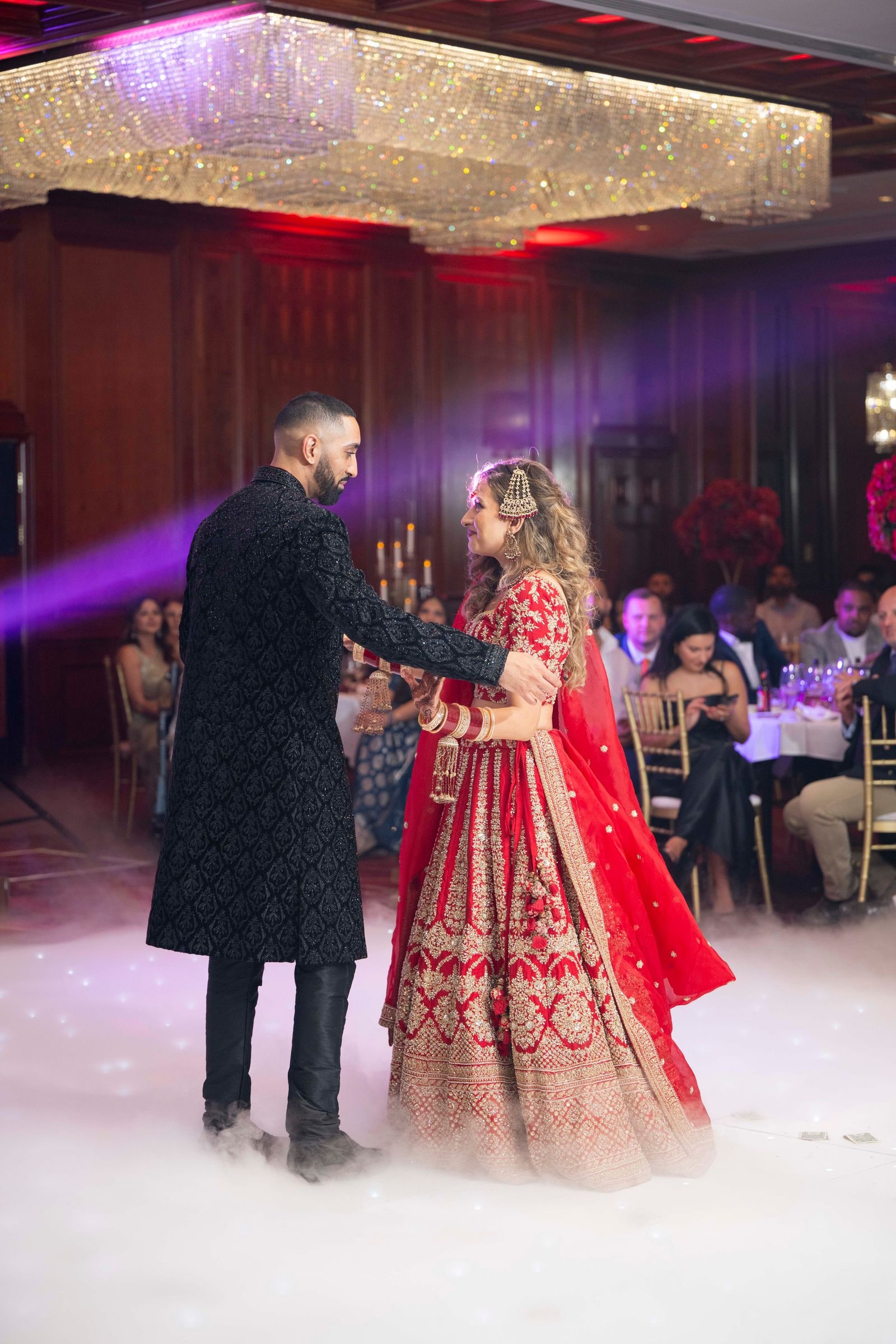 First dance on a cloud of dry ice beneath a gold-lit ceiling, guests at their tables