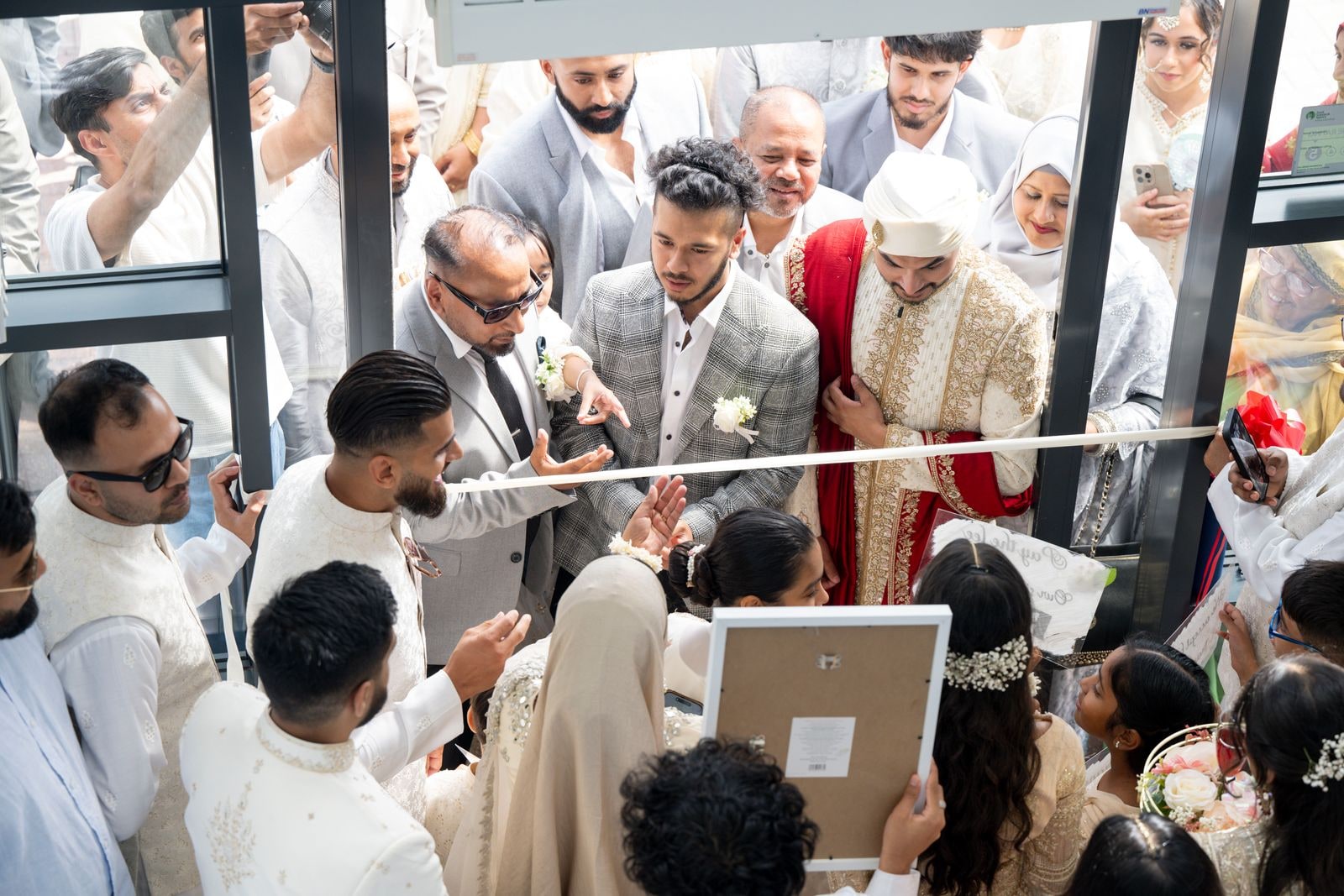 Guests crowding round the groom at the entrance, phones raised, as he is welcomed in