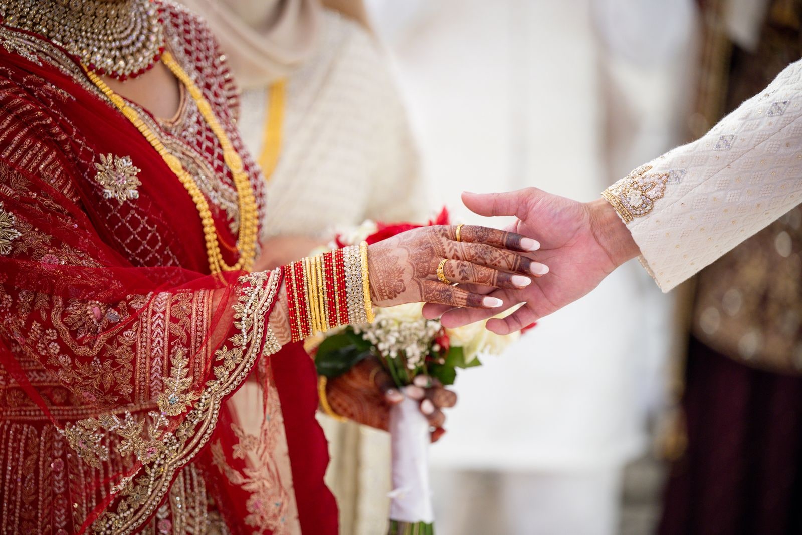The groom's hand reaching for his bride's during the ceremony, her bangles gold and red