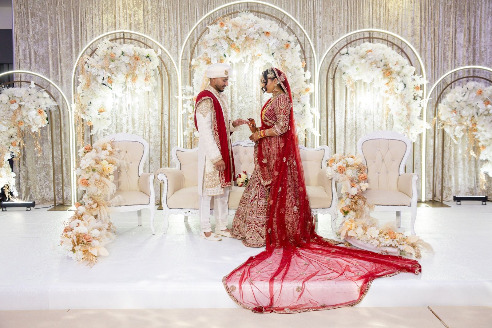 Groom leading his bride across the stage, her red train sweeping behind