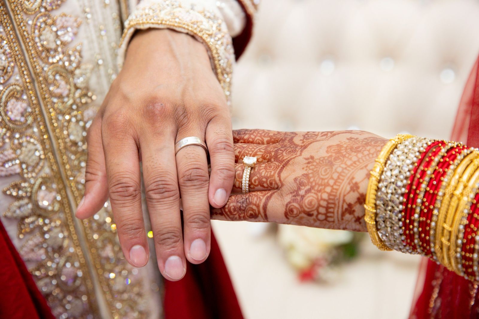 The groom's hand with his new ring resting over his bride's hennaed hand and gold bangles