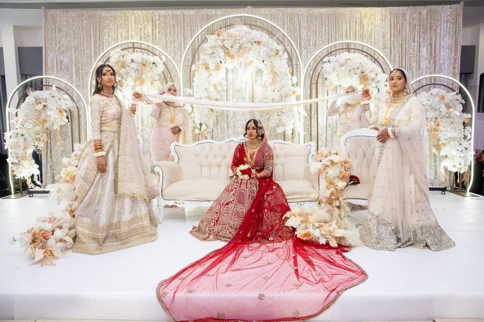Bride seated on the stage sofa while women in cream arrange her train