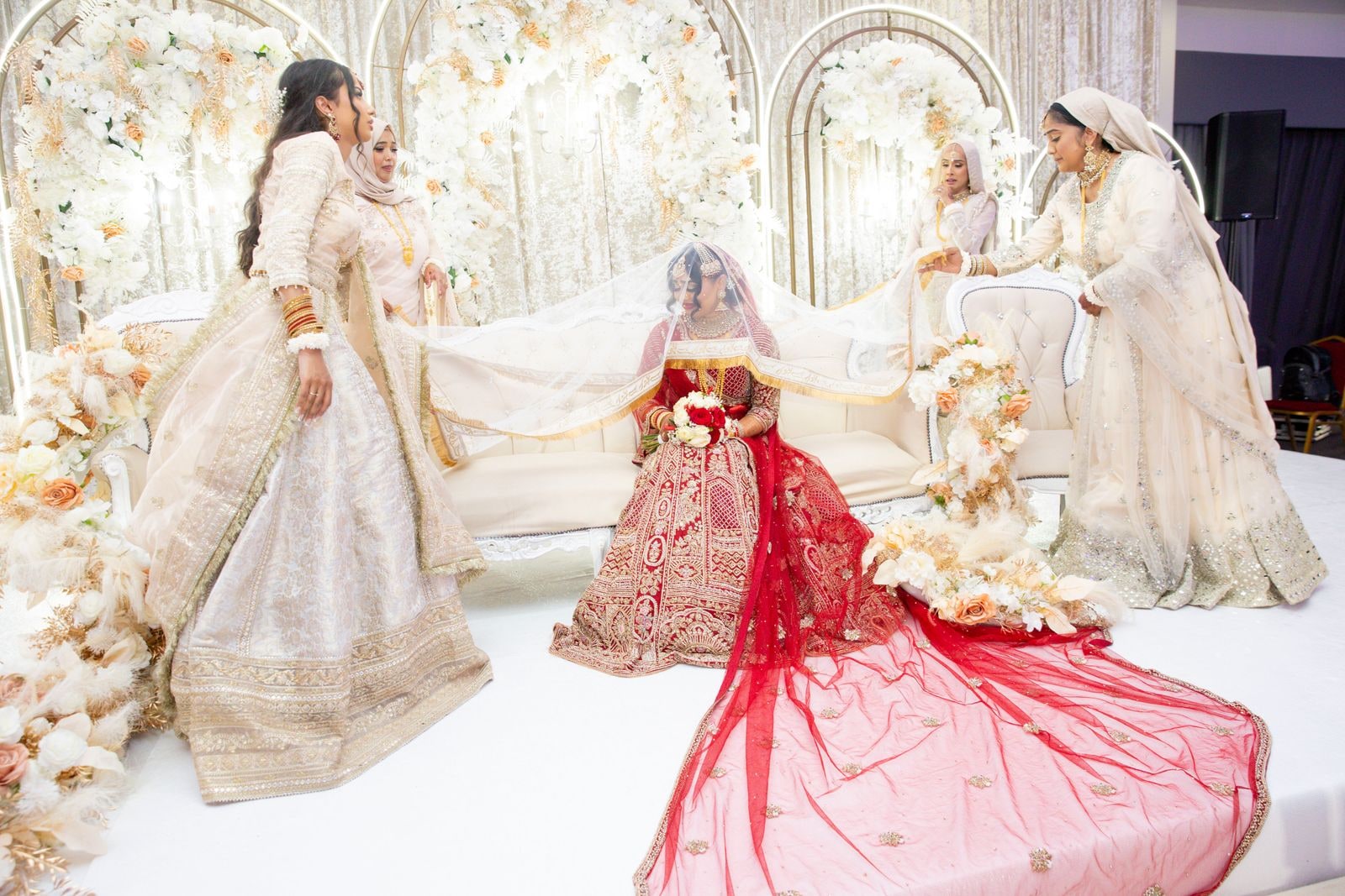 Bride seated alone in red on the white stage, her family standing to either side